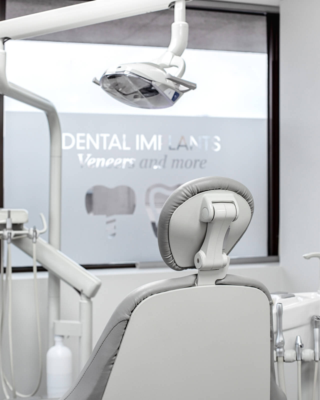 Empty dental chair in a dental clinic with overhead light and signage in the background.