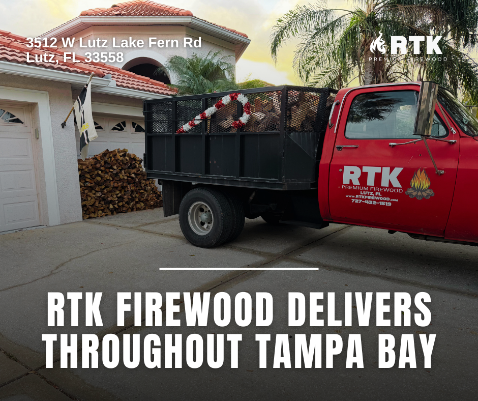 A red truck with 'RTK Firewood' logo on the door and a black cargo bed filled with firewood, parked in front of a white house with a tiled roof in Tampa Bay area, Florida, during daytime. Piles of firewood are stacked against the house. Outdoor palm 