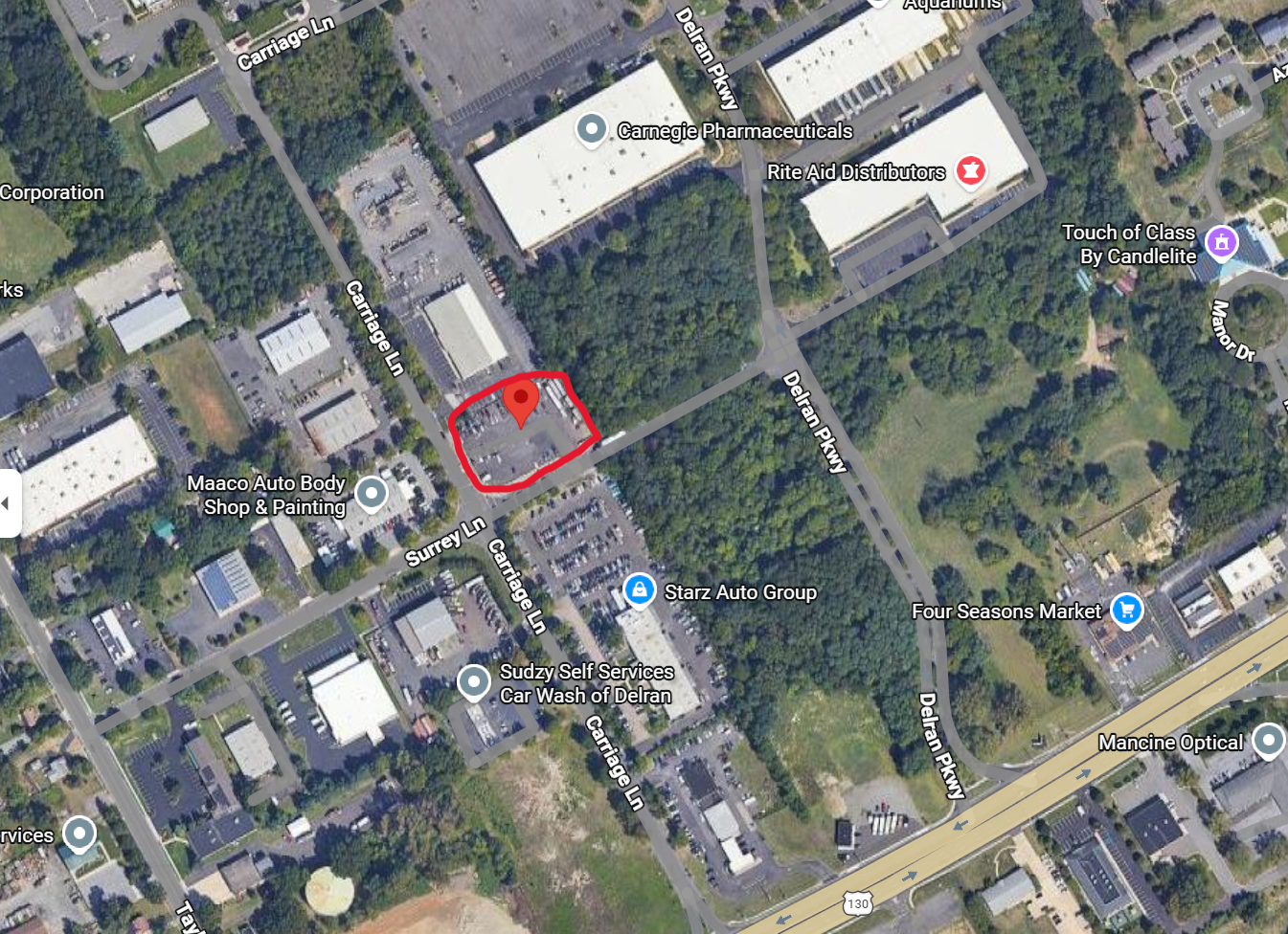 Satellite map showing commercial and industrial areas, with labels for businesses, roads, and a shaded parking lot area outlined in red.