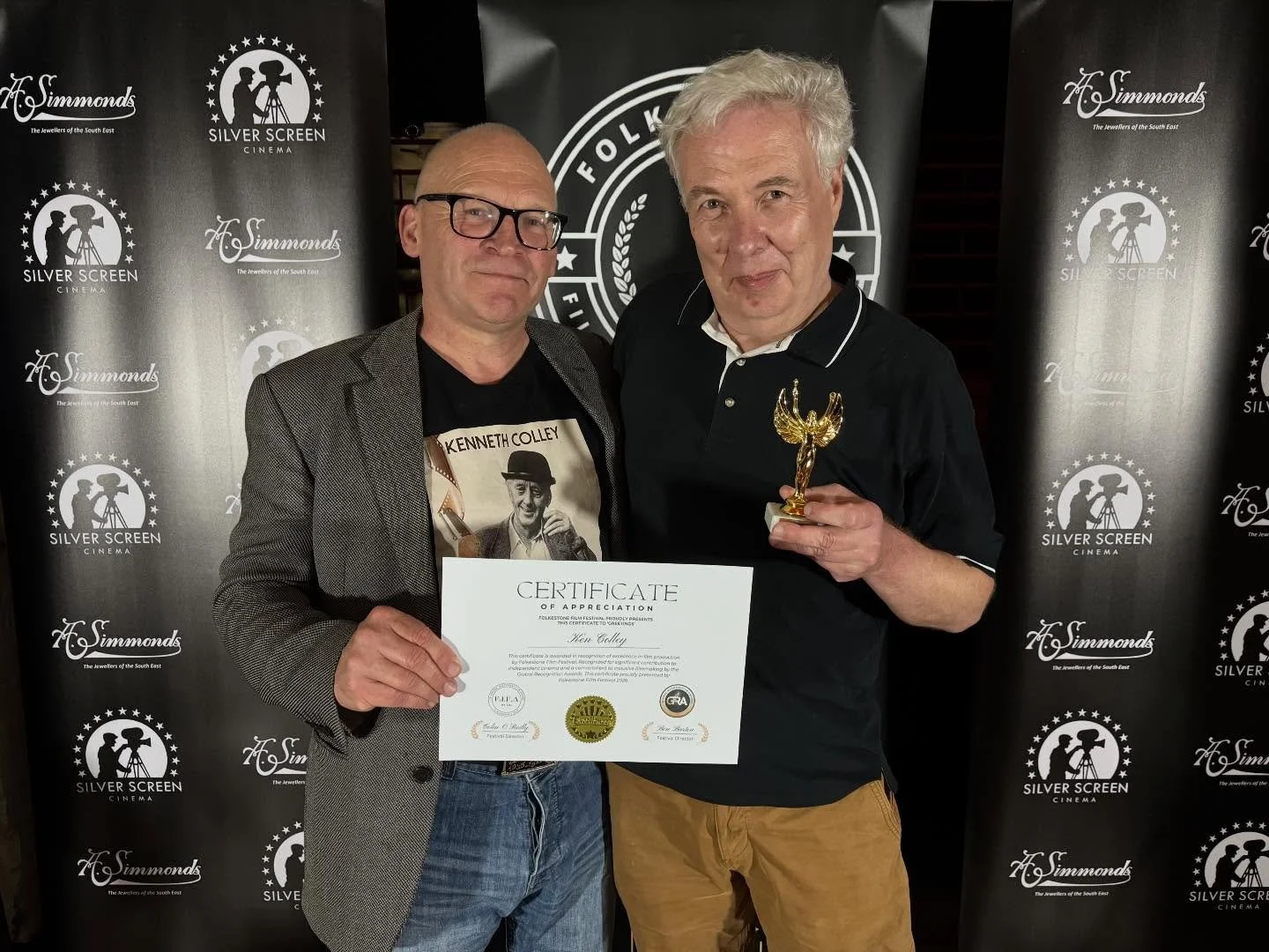 Two men holding a certificate and a trophy at a film festival