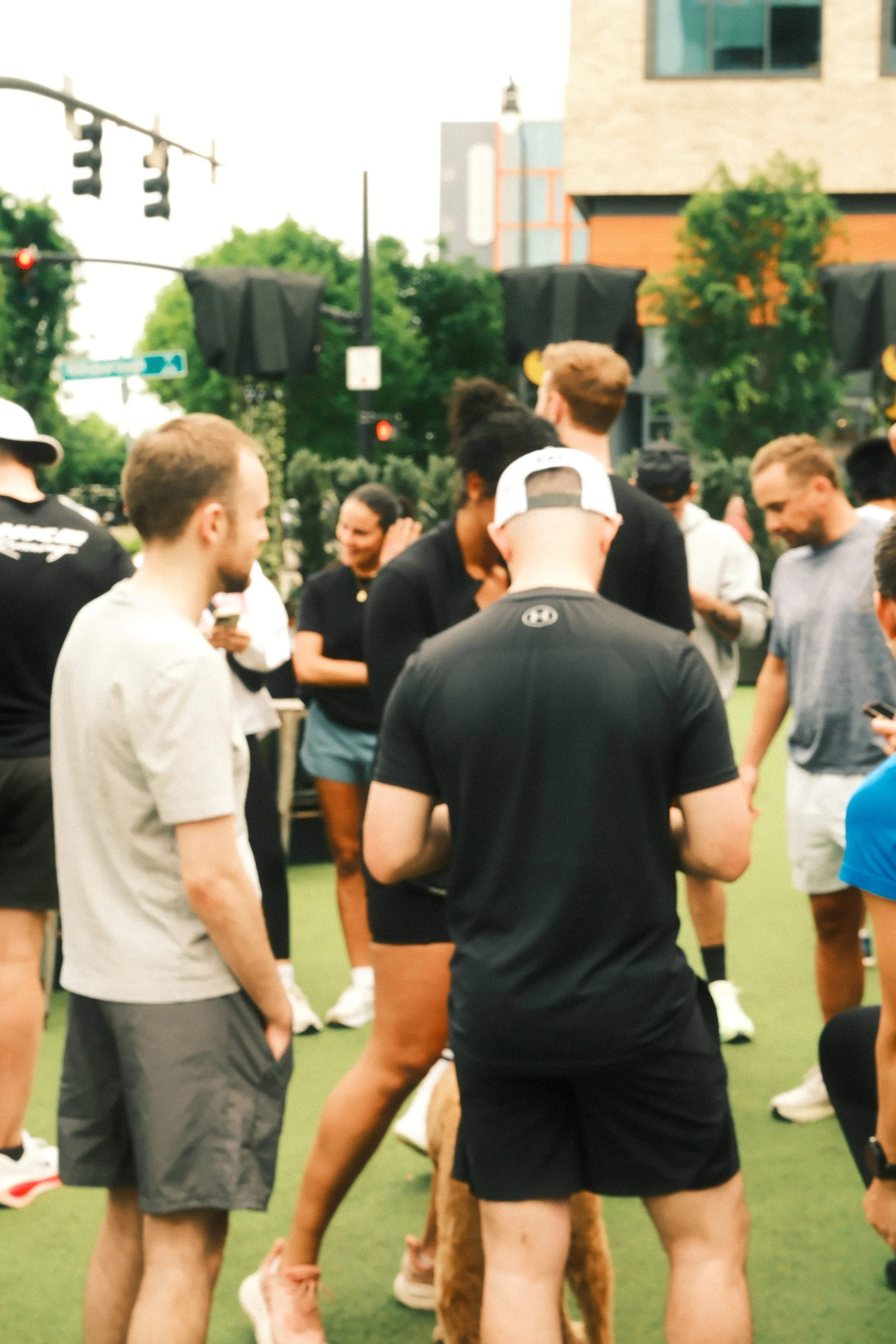 A group of young people gathered outdoors on a green field, likely for a sports event, with some individuals talking and others looking at a device.