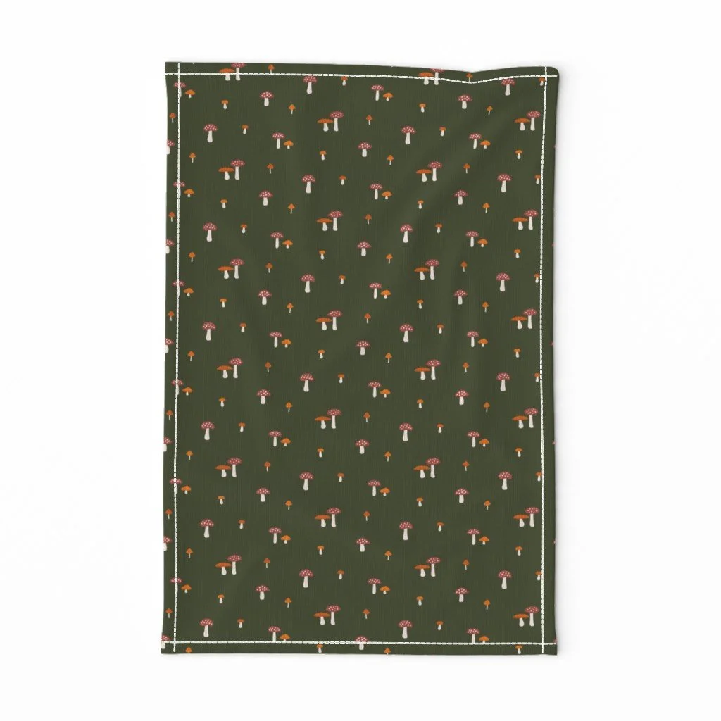 Fall mushroom tea towel in dark forest green, scattered with rusty red and pumpkin orange toadstools — a cozy kitchen accent for autumn.