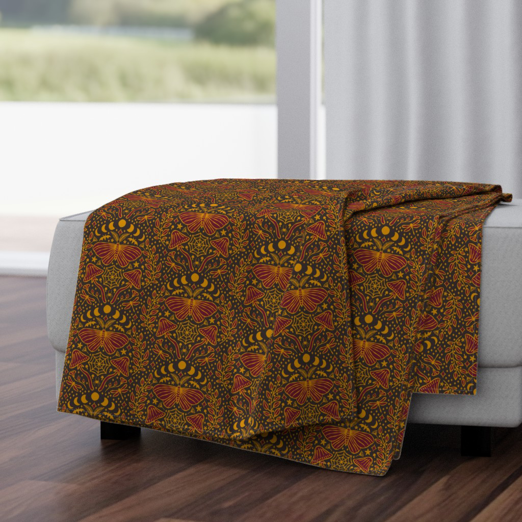 Gold and dark wine moth & mushroom damask throw blanket, draped for a cozy nighttime-garden living room.