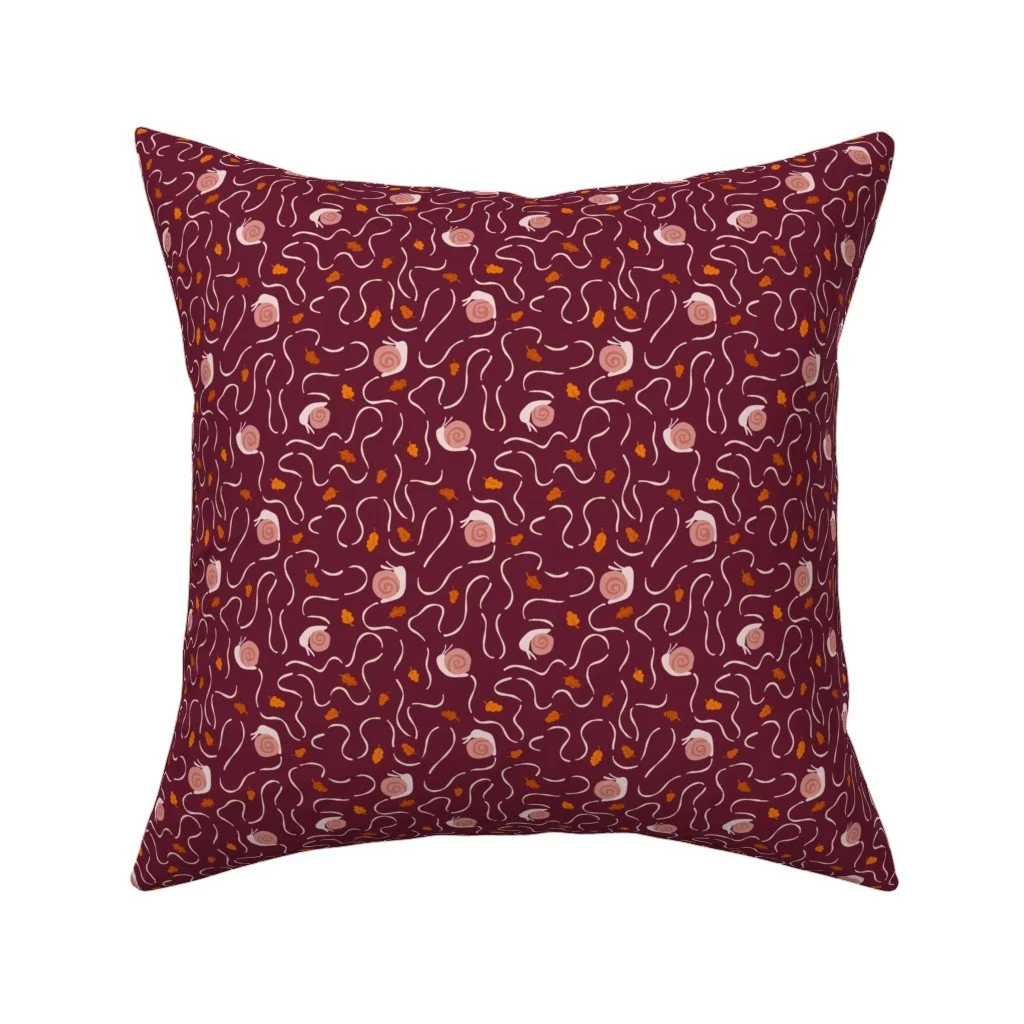 Snails and trails throw pillow in dark plum, with blush pink snails on curling cream trails — a whimsical fall accent for a reading chair or sofa.