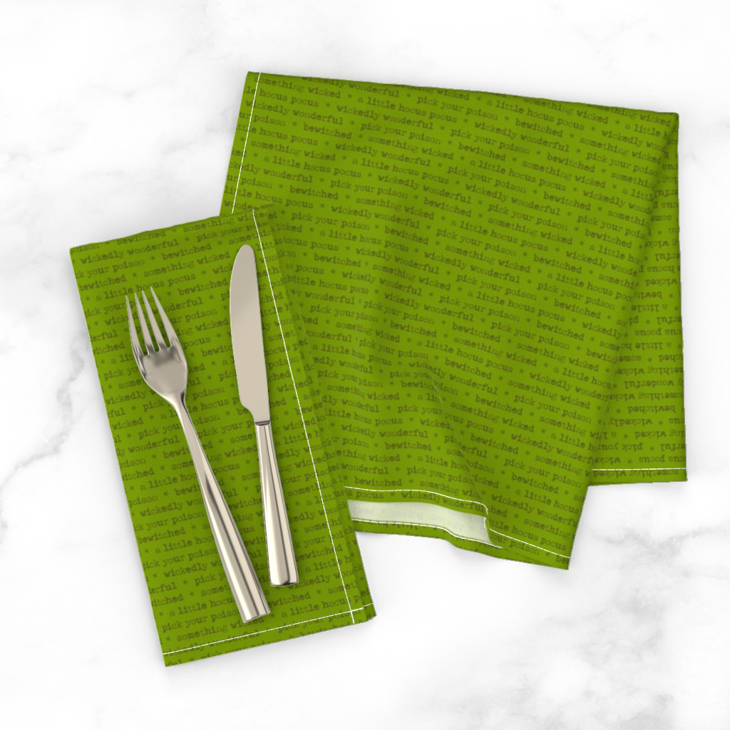 Cloth napkins in the witchy phrase print, dark green typewriter lettering on a green ground.