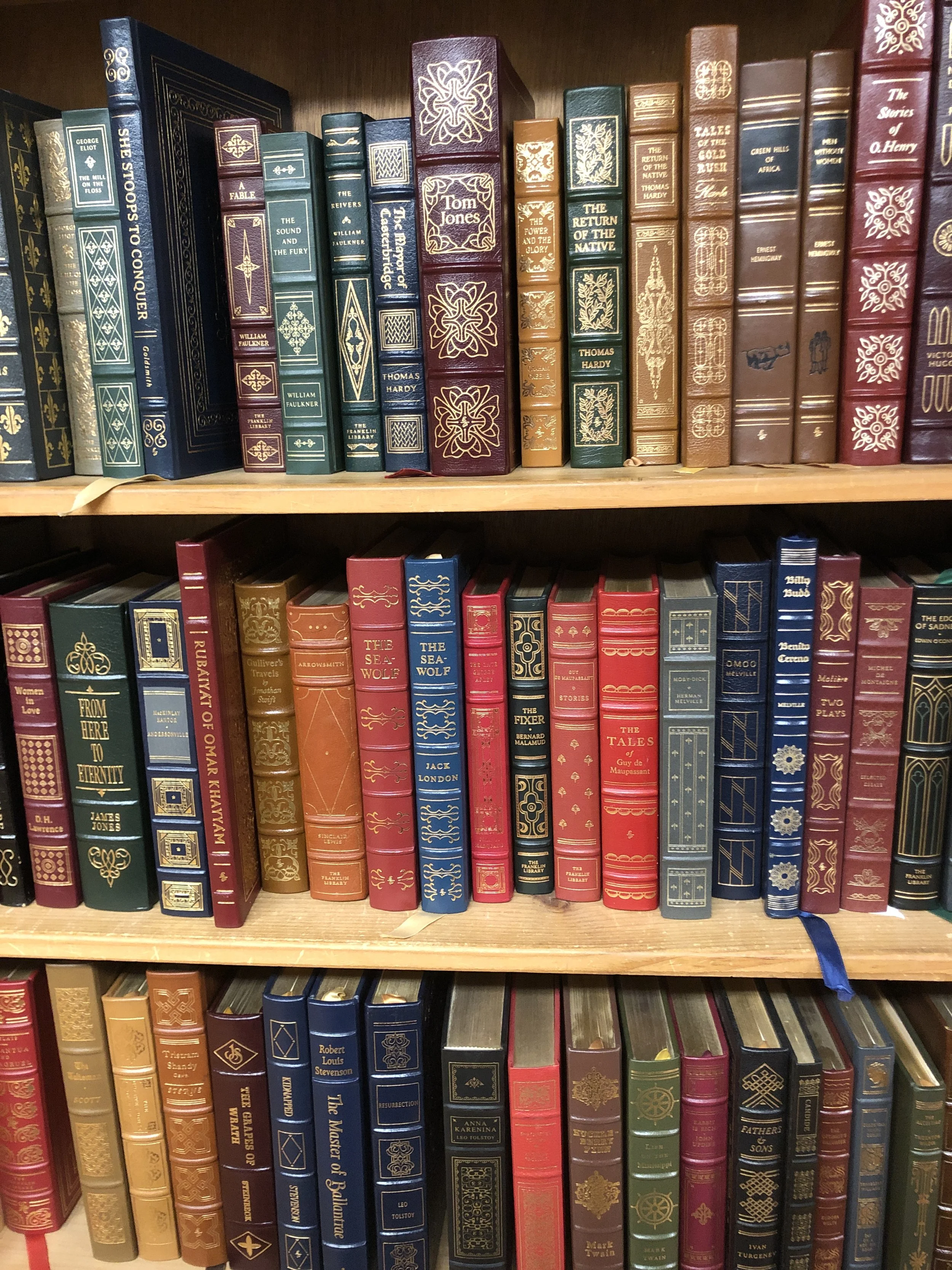 A bookshelf filled with an assortment of colorful hardcover books, some with gold or decorative detailing on the spines.