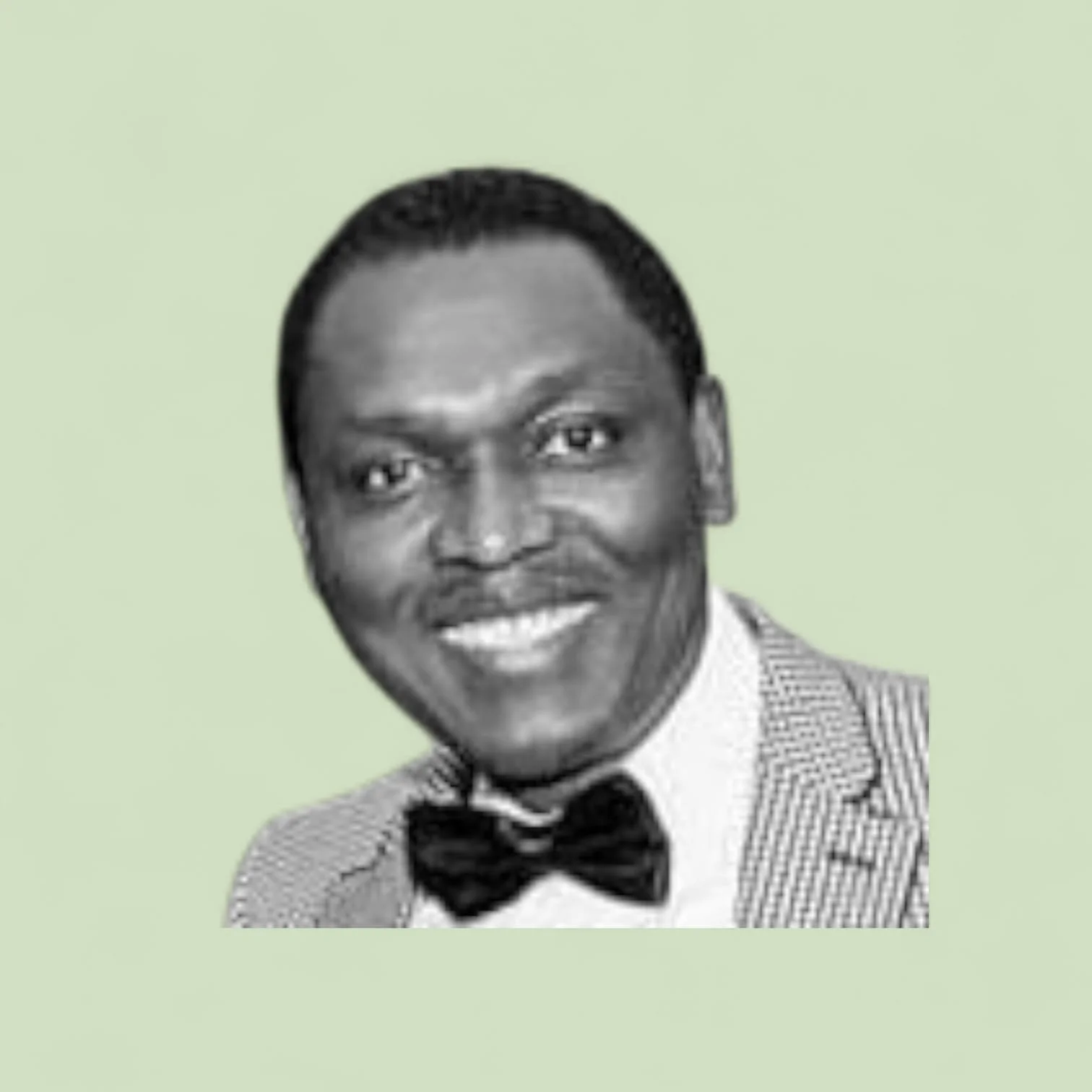 Black and white photo of a smiling man in a tuxedo, with a light green background.