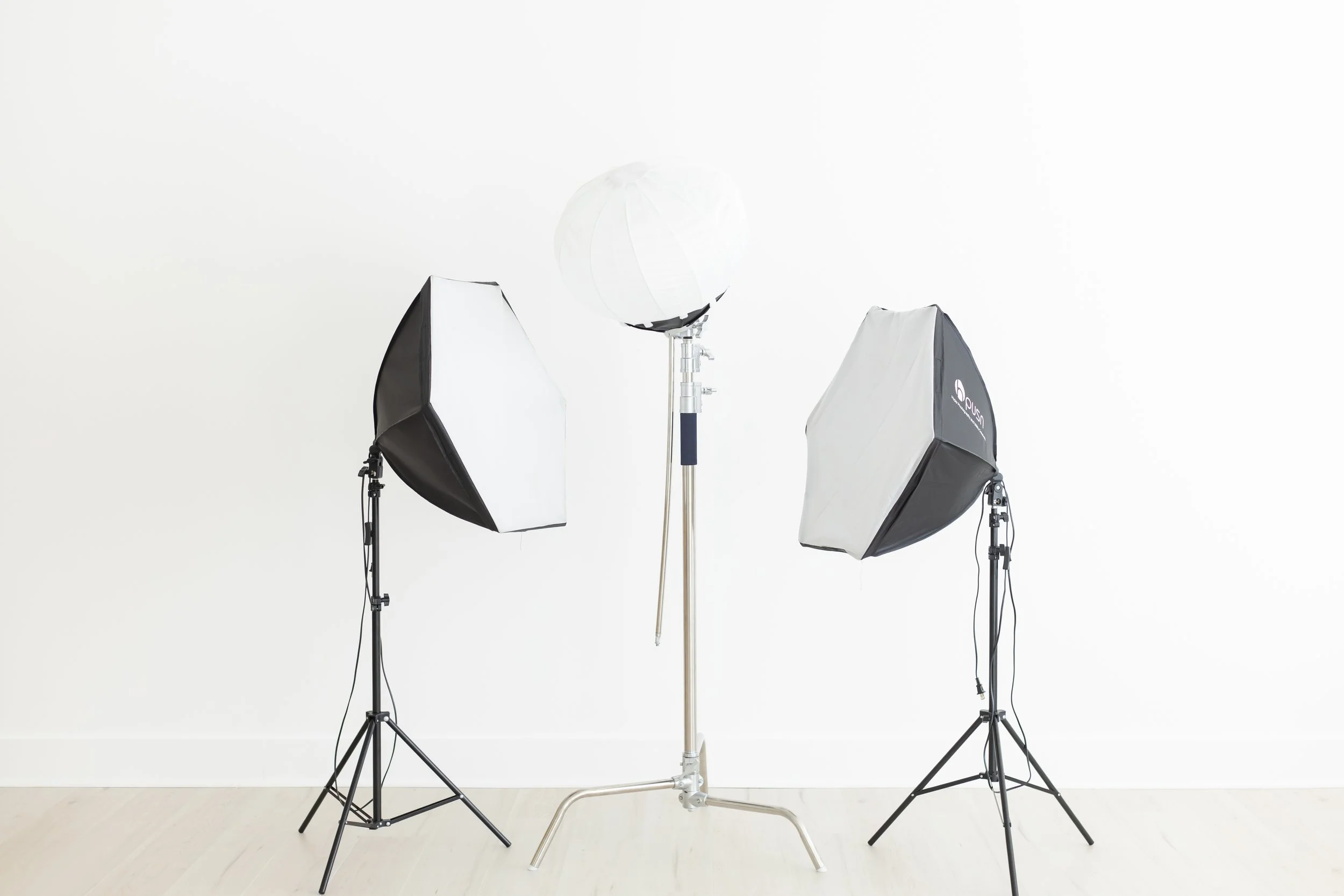 Studio photography setup with three softbox lights and an umbrella light in front of a white wall.
