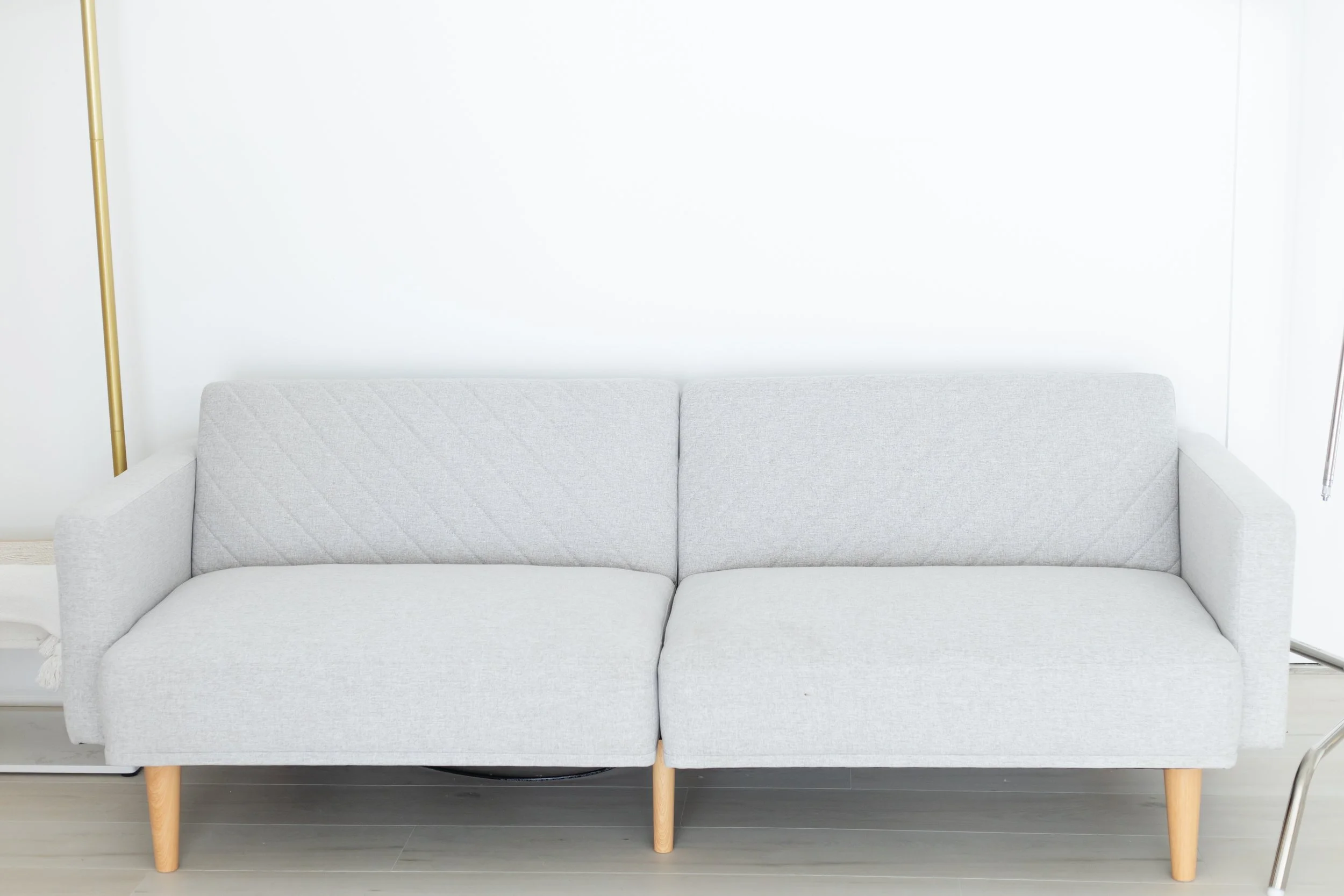 A light gray sofa with wooden legs placed against a plain white wall in a minimalist room.