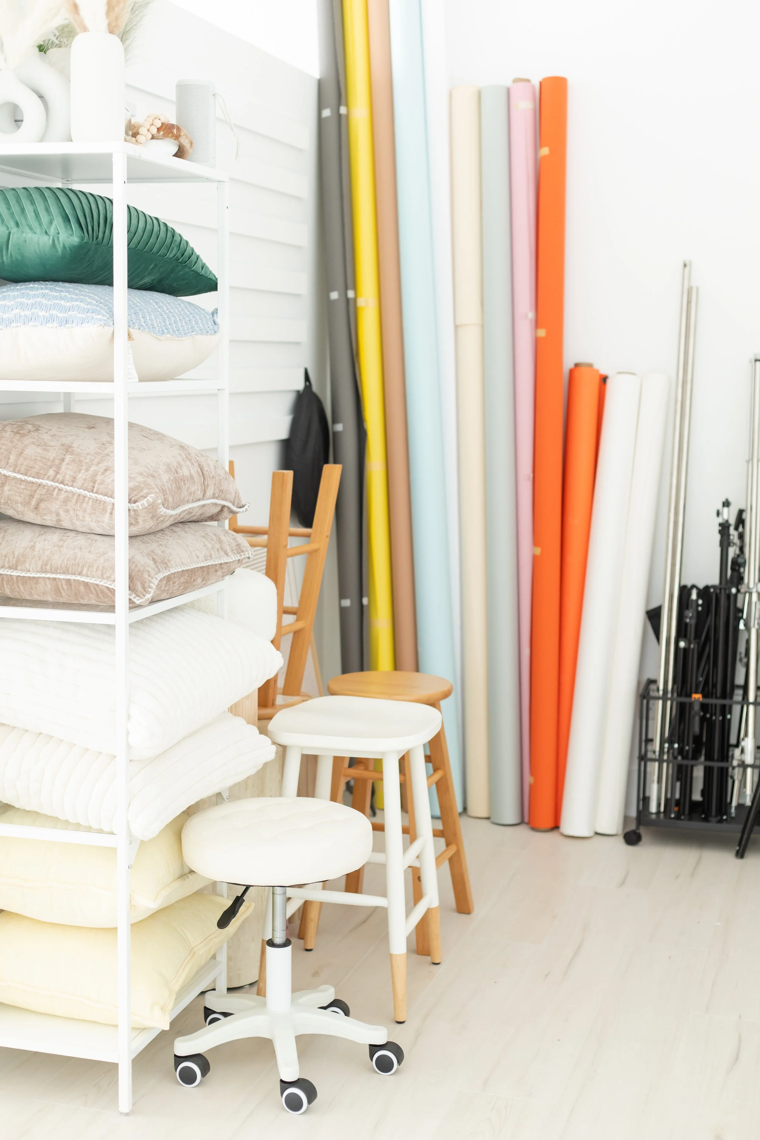Display of fabric rolls in different colors and patterns, stacked on a white shelf, with various pillows and small furniture nearby in a bright, neatly organized room.