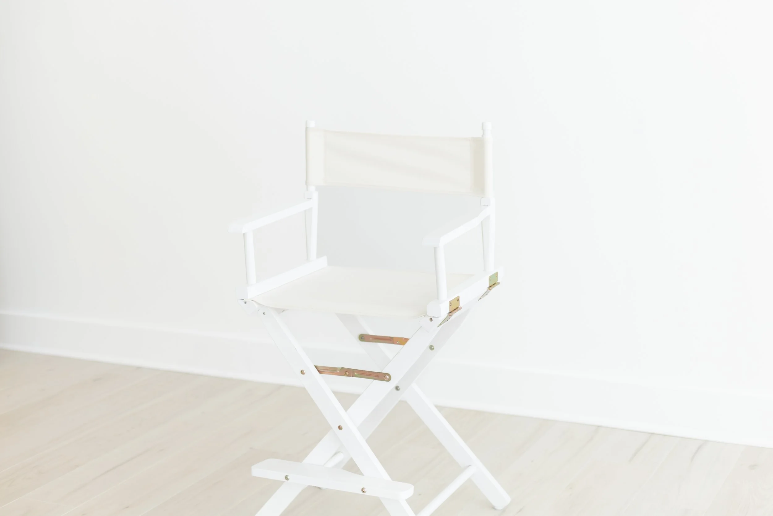 A white director's chair set against a plain white wall and light-colored floor.
