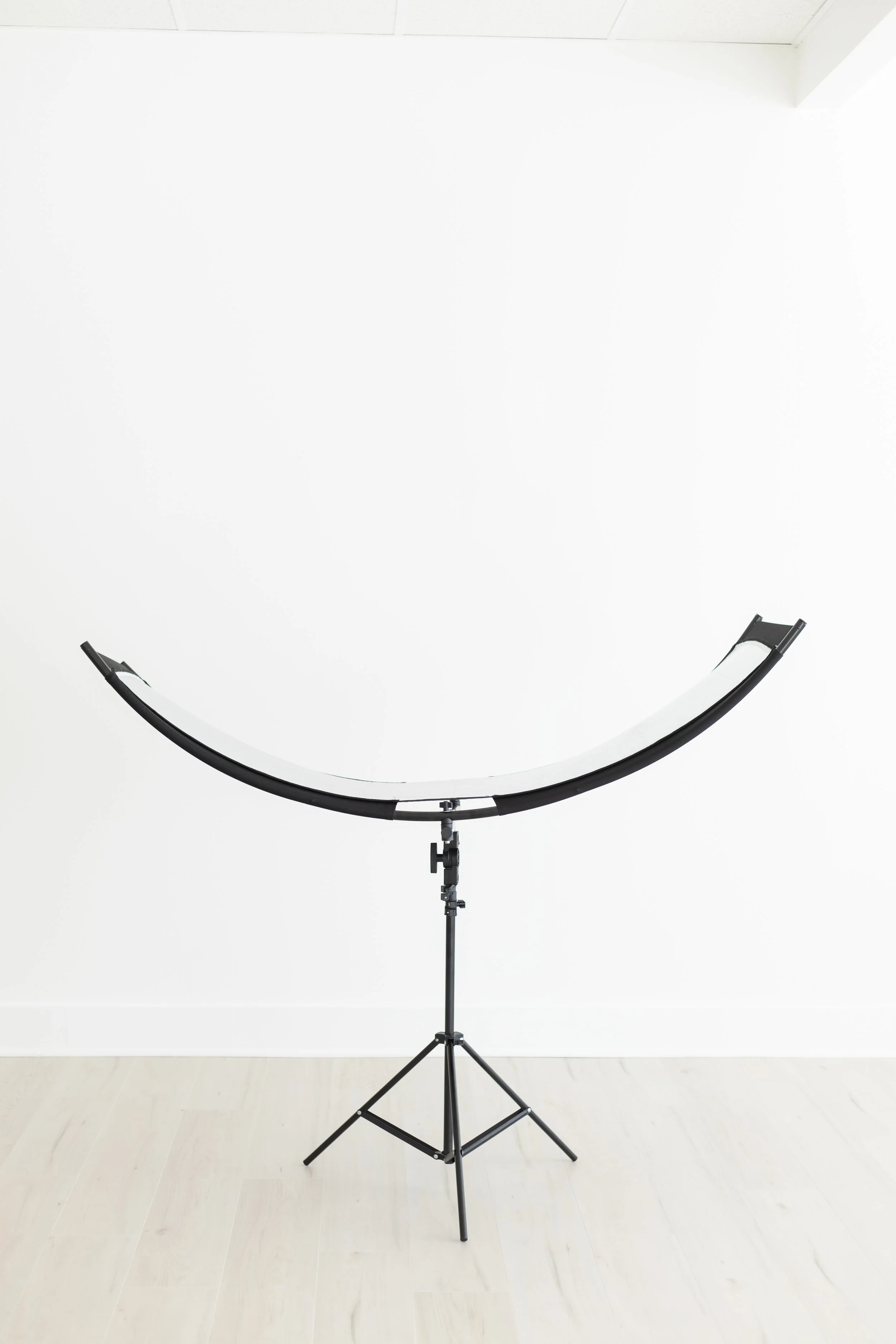 Photography light stand and curved reflector panel in a white room with light-colored floor.