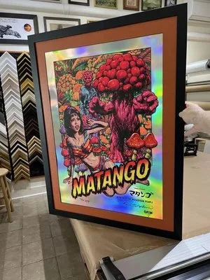 Colorful framed poster titled 'Matango' featuring a woman pointing at a large mushroom with smaller mushrooms nearby, set in a vibrant, psychedelic background.  custom framing brookline pictureplacebrookline.com