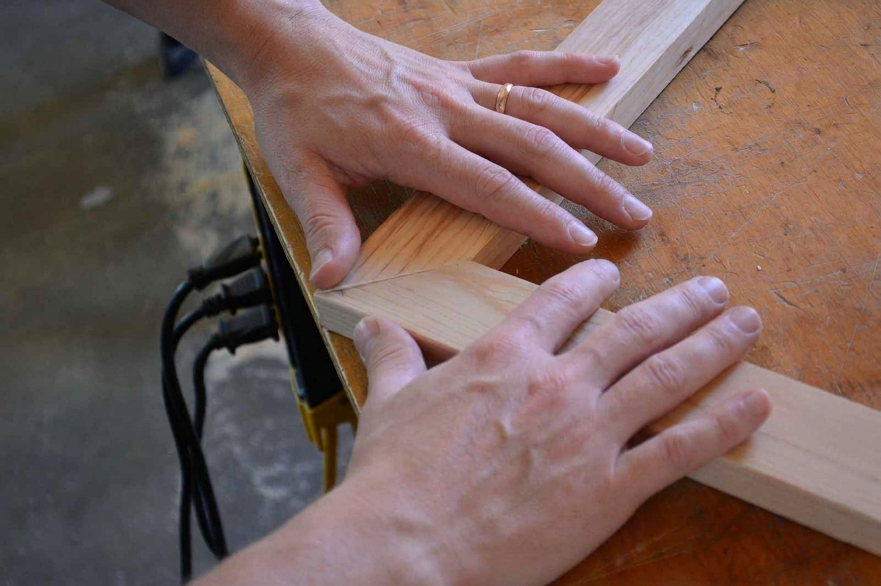 Close-up of hands assembling wooden corner joint on workbench in woodworking workshop.