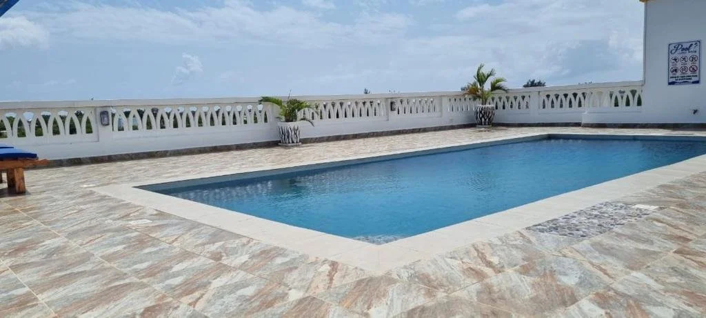 Swimming pool on a rooftop terrace with white decorative railing, potted plants, and a sign indicating pool rules.