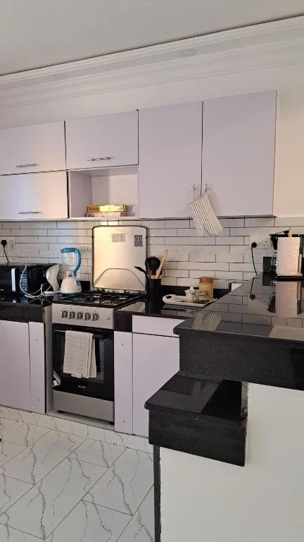 Kitchen with white cabinets, black countertops, white tiled backsplash, and various appliances including a stove, microwave, toaster, and coffee maker.