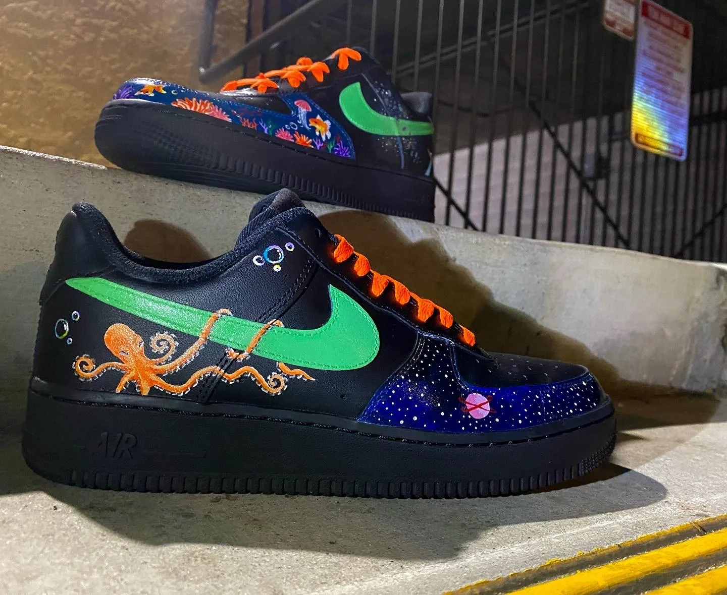 A pair of decorated Nike sneakers with a space and ocean theme, featuring octopus and starry designs, placed on a concrete step.