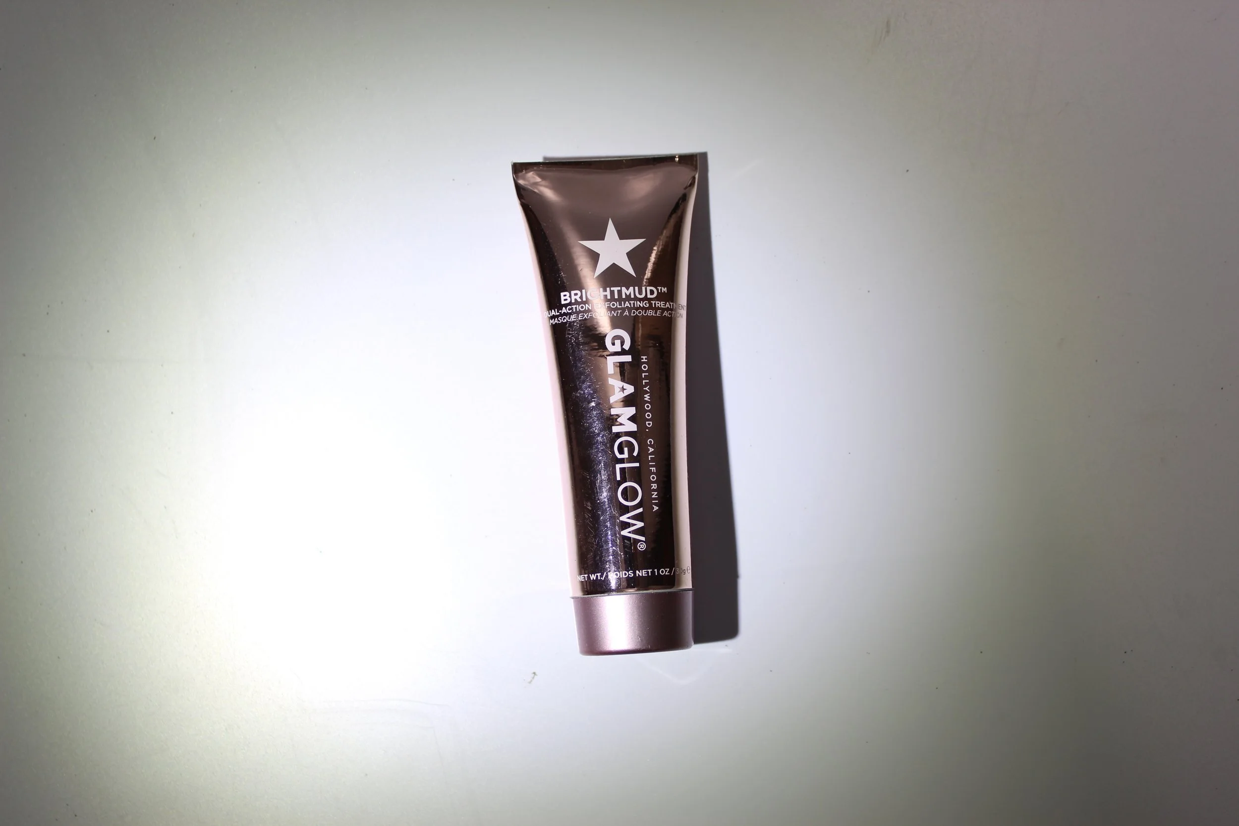 A tube of Brightmud Glam dual-action exfoliating treatment with a star logo on a light surface.