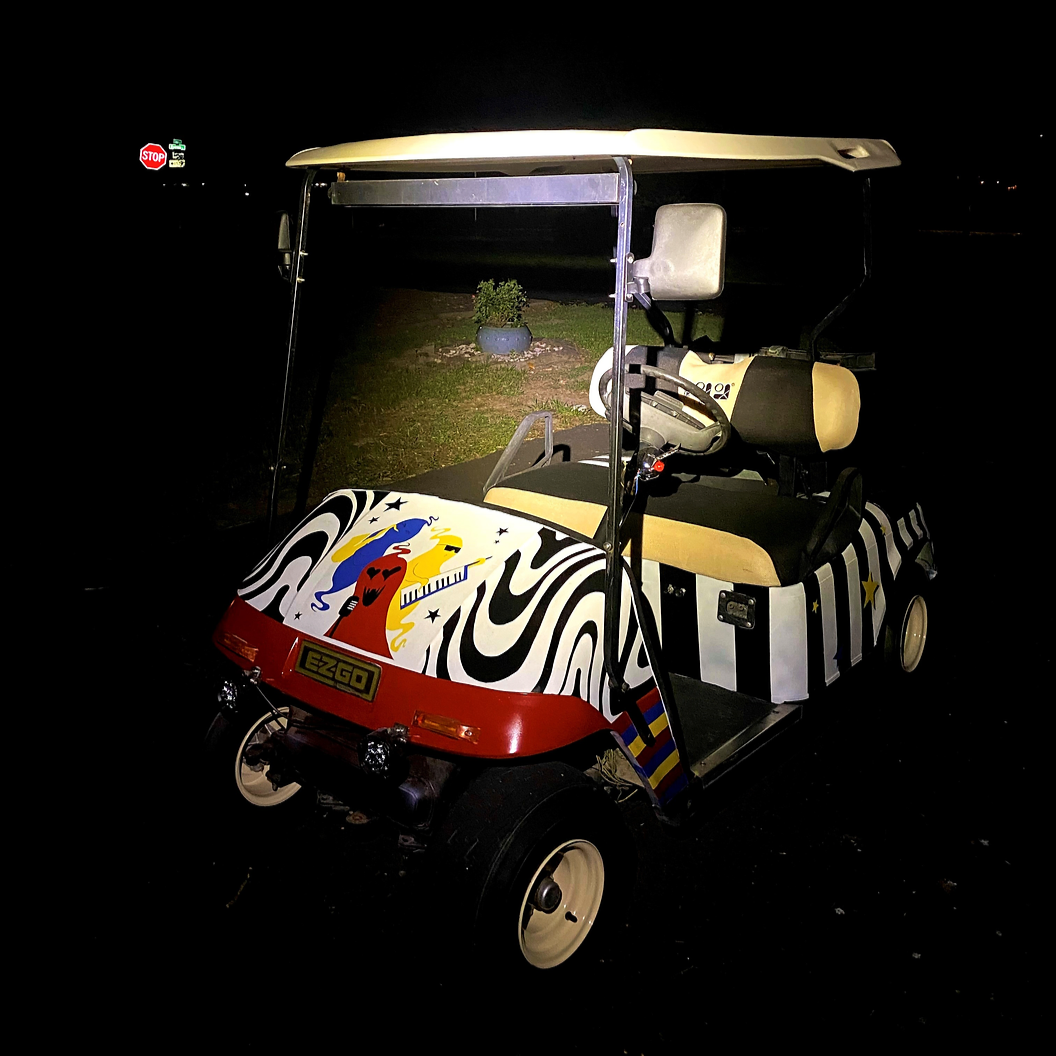 Colorful custom-designed golf cart with rainbow, musical notes, zebra stripes, and abstract art, parked outdoors at night.