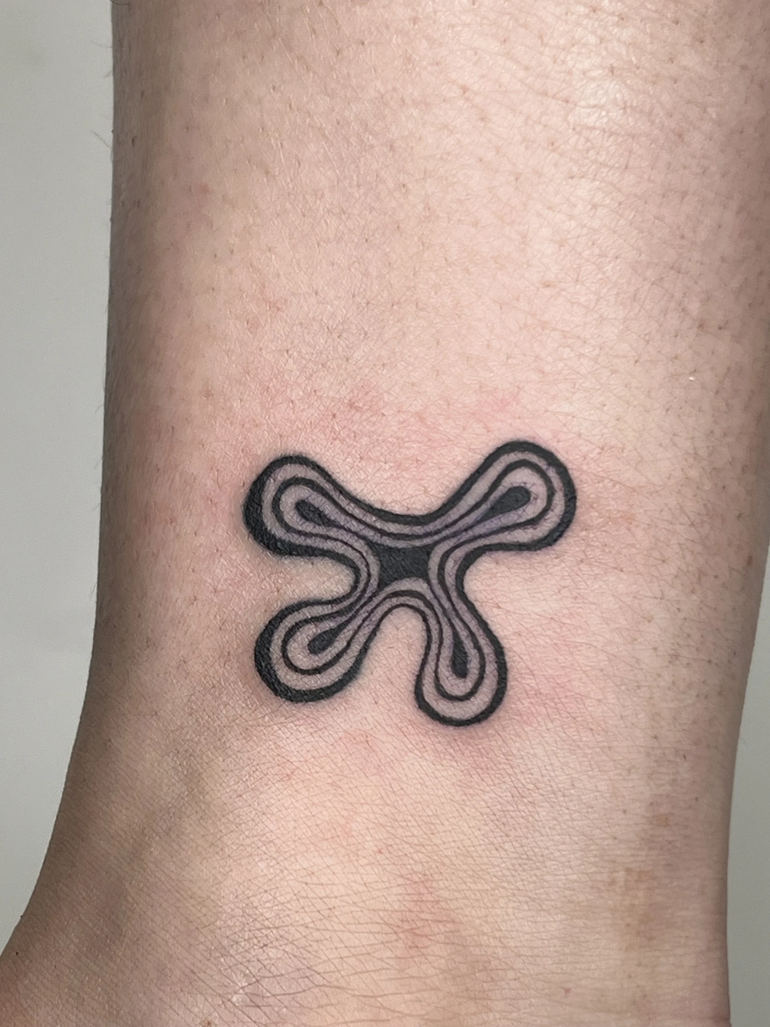 Close-up of a person's skin with a black ink tattoo of a star-shaped cross with looped sides.