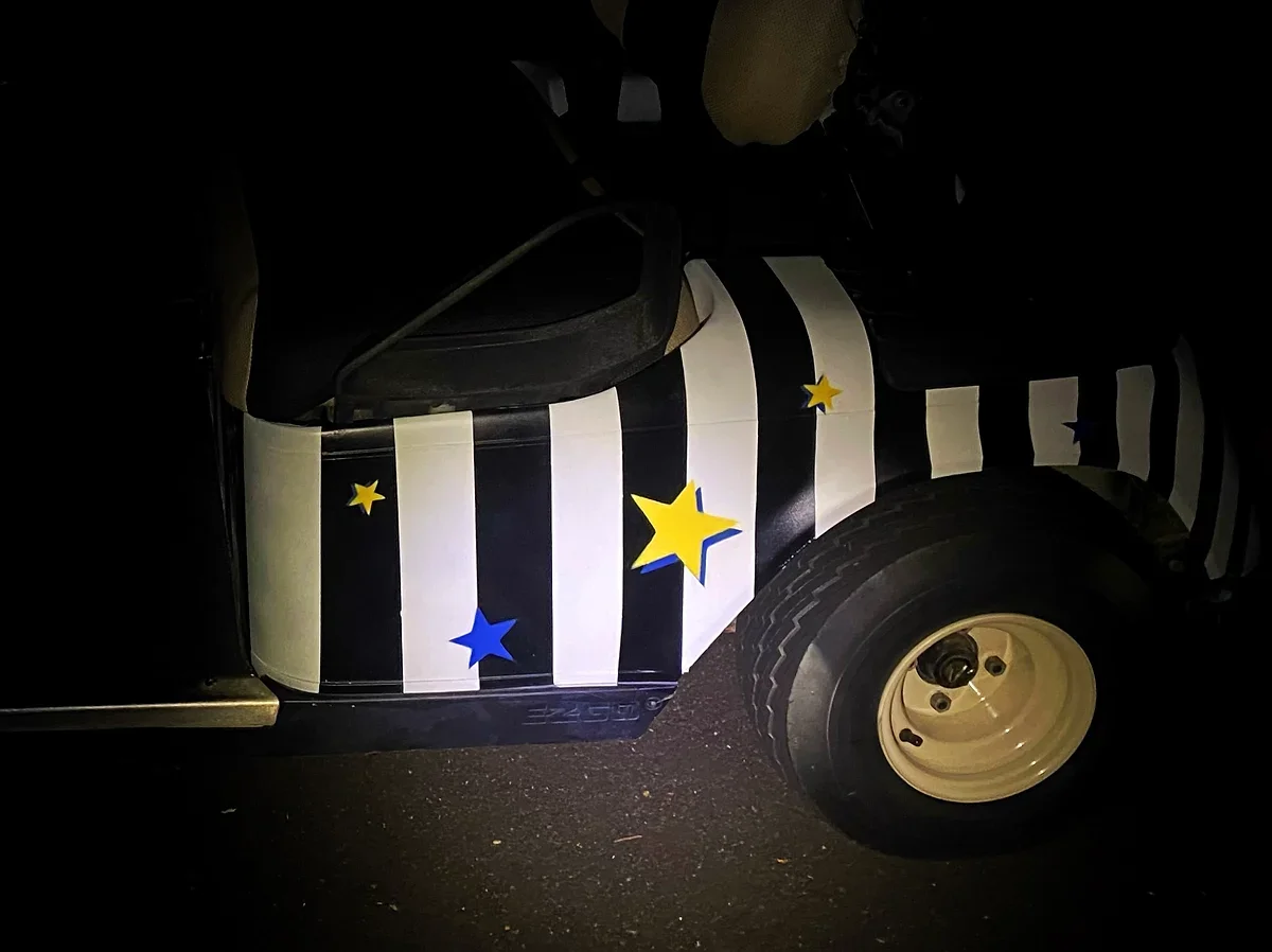 A golf cart with black and white vertical stripes and star-shaped decorations in blue and yellow, parked on asphalt at night.