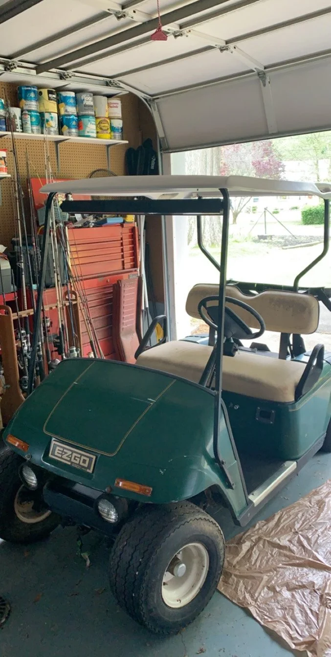 Green EZGO golf cart parked inside a garage, with tools and shelves in the background.