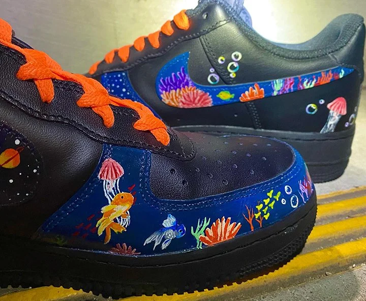 Pair of black sneakers decorated with colorful underwater sea life including fish, coral, jellyfish, and bubbles, with orange shoelaces.