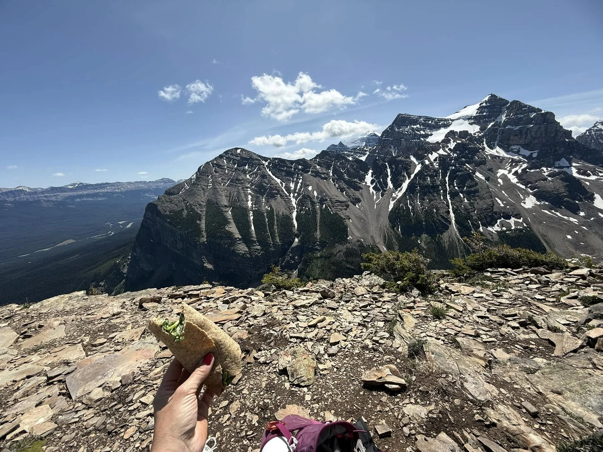 Person holding a breakfast burrito with mountain and sky in the background.