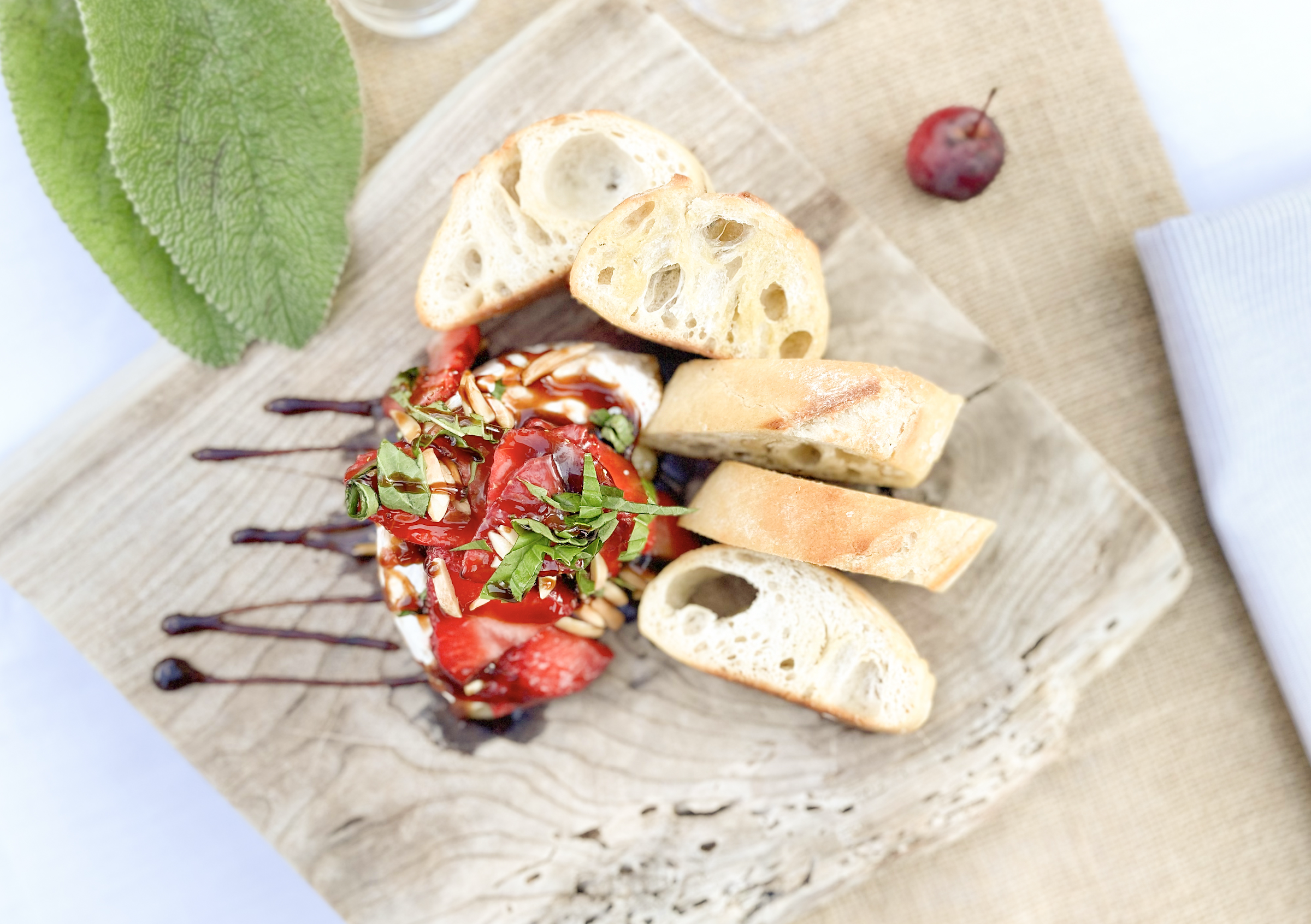 Assorted appetizers on a wooden board, including slices of bread, strawberries, and a dipping sauce with chopped nuts and herbs.