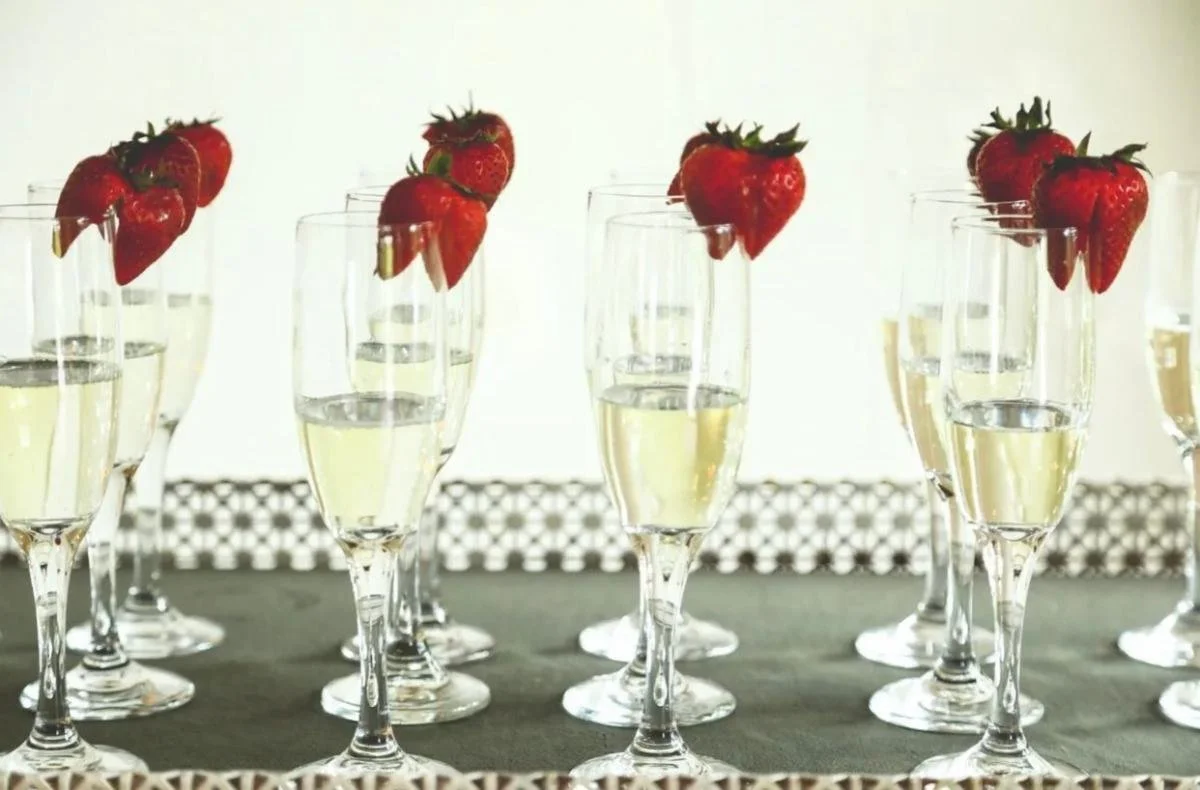 Multiple champagne glasses decorated with strawberries, set on a table.
