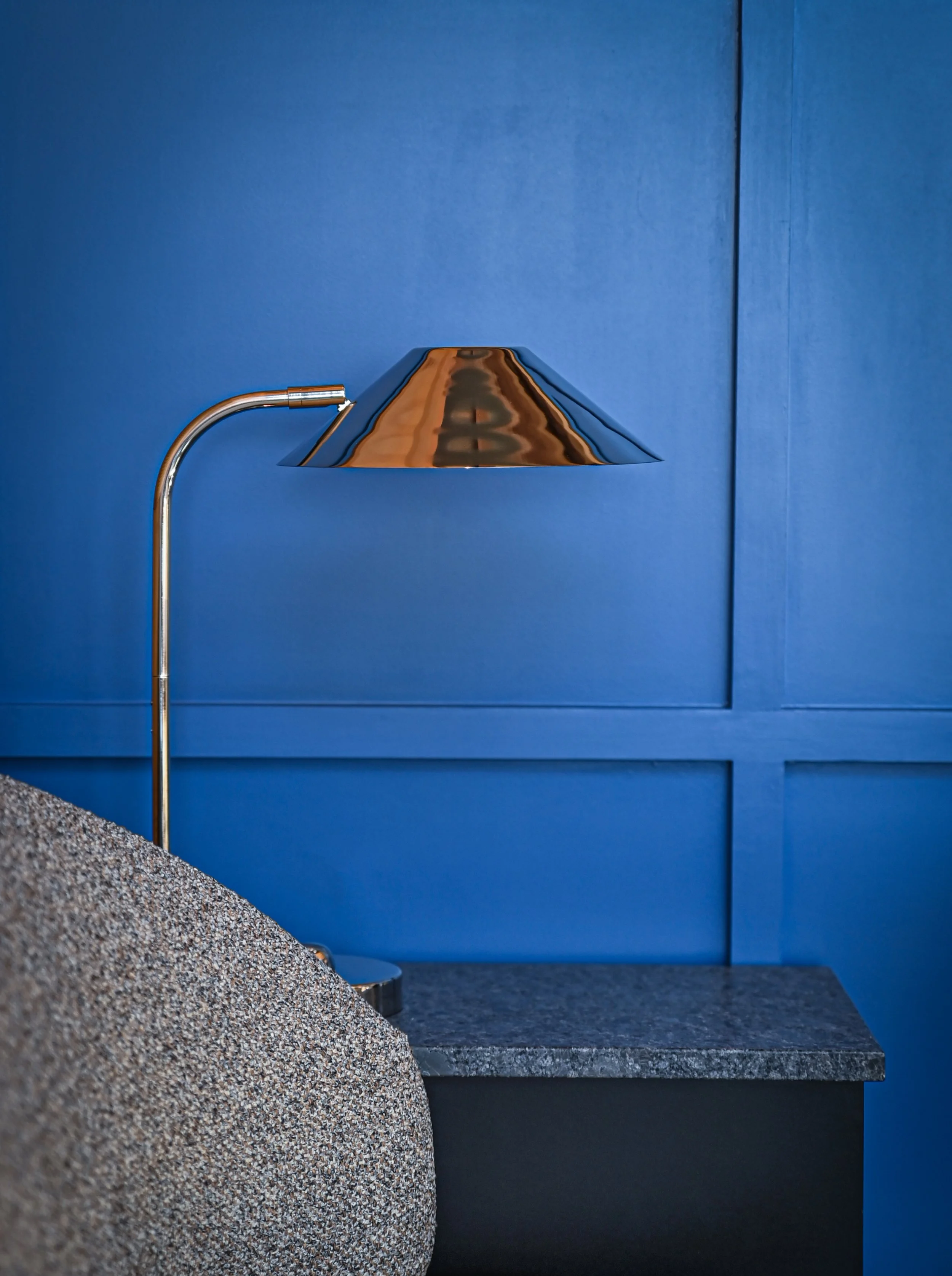 A modern wall sconce with a reflective metallic finish mounted on a blue wall, with a granite surface in the foreground.