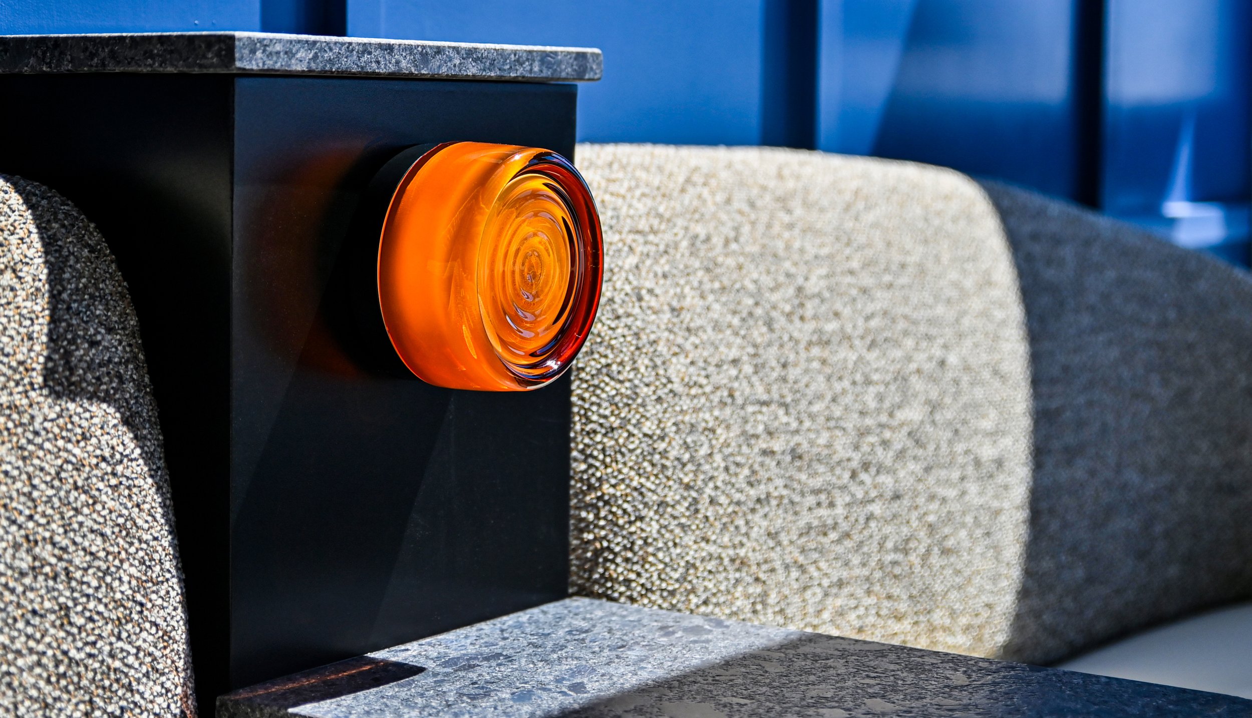 Close-up of an orange circular glass reflector attached to a black metal surface with a speckled gray granite background.