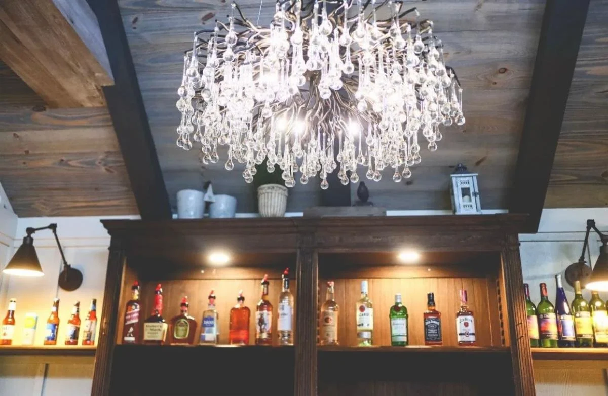 A luxurious chandelier with hanging glass crystals over a bar area with various bottles of alcohol on shelves.