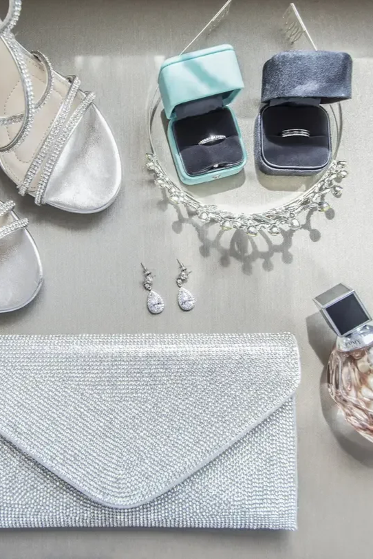 Jewelry and accessories displayed on a table, including a silver clutch, a pair of teardrop earrings, a necklace, a perfume bottle, and two jewelry boxes with rings.