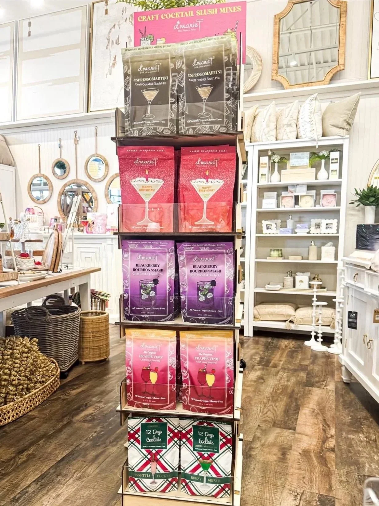 A display rack with various packet mixes for craft cocktails and slush drinks in a store with cozy decor, mirrors, and shelves with home accessories.