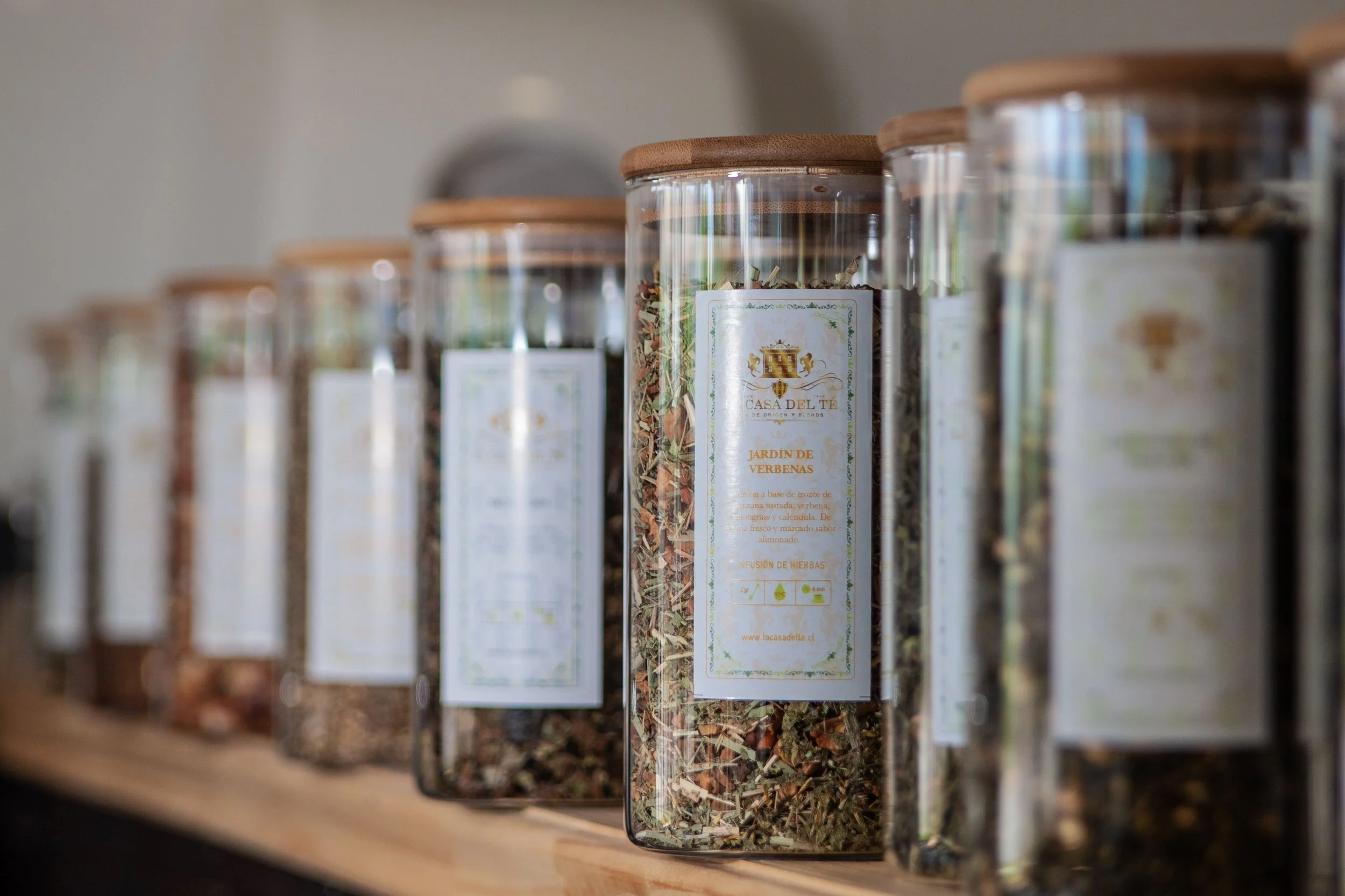 A selection of glass jars filled with herbal teas displayed on an indoor shelf.