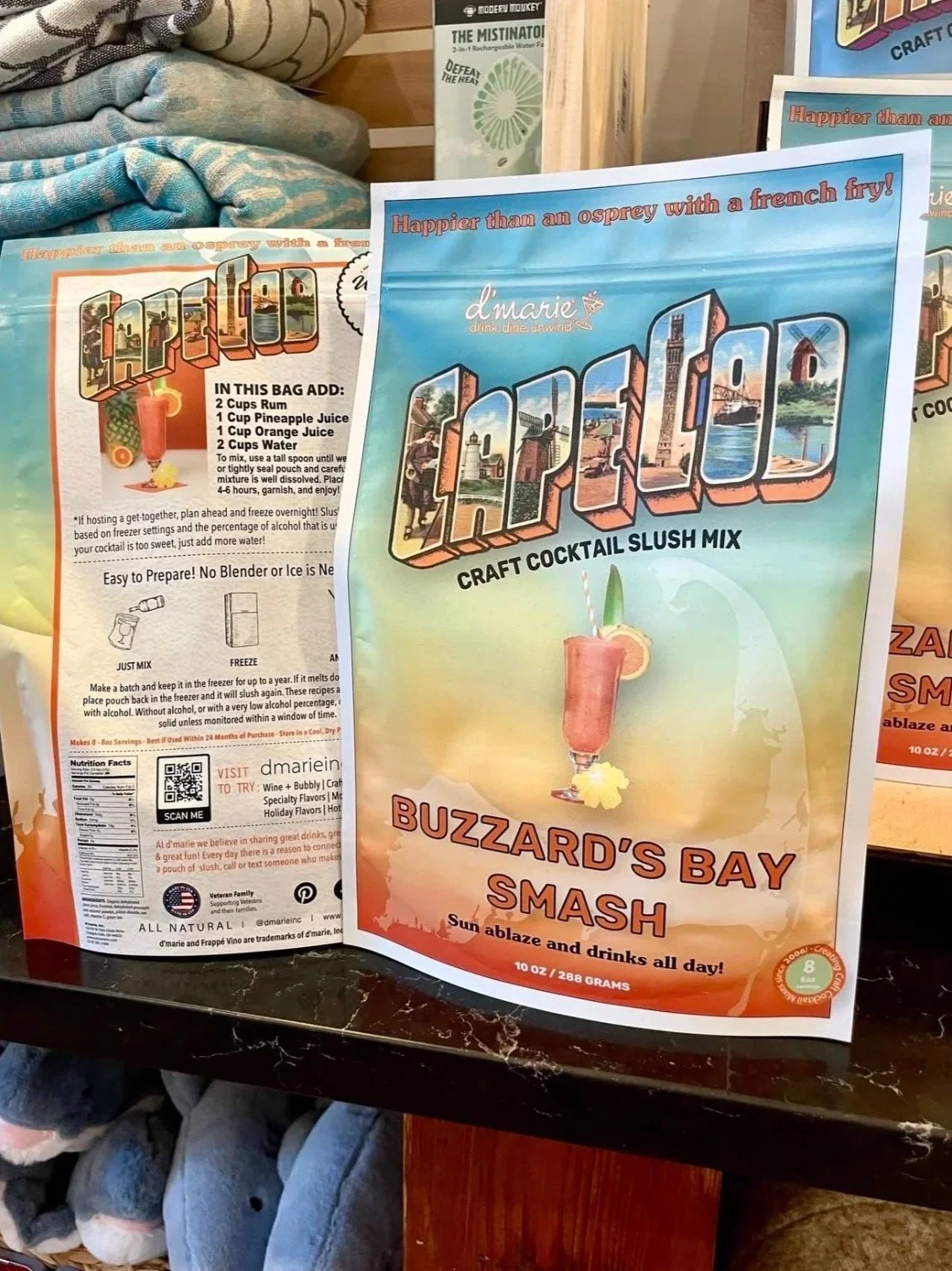 A colorful flyer for Buzzard's Bay Smash craft cocktail slush mix, featuring a tropical theme with blurred background of a beach scene and a pink cocktail drizzled with pineapple.