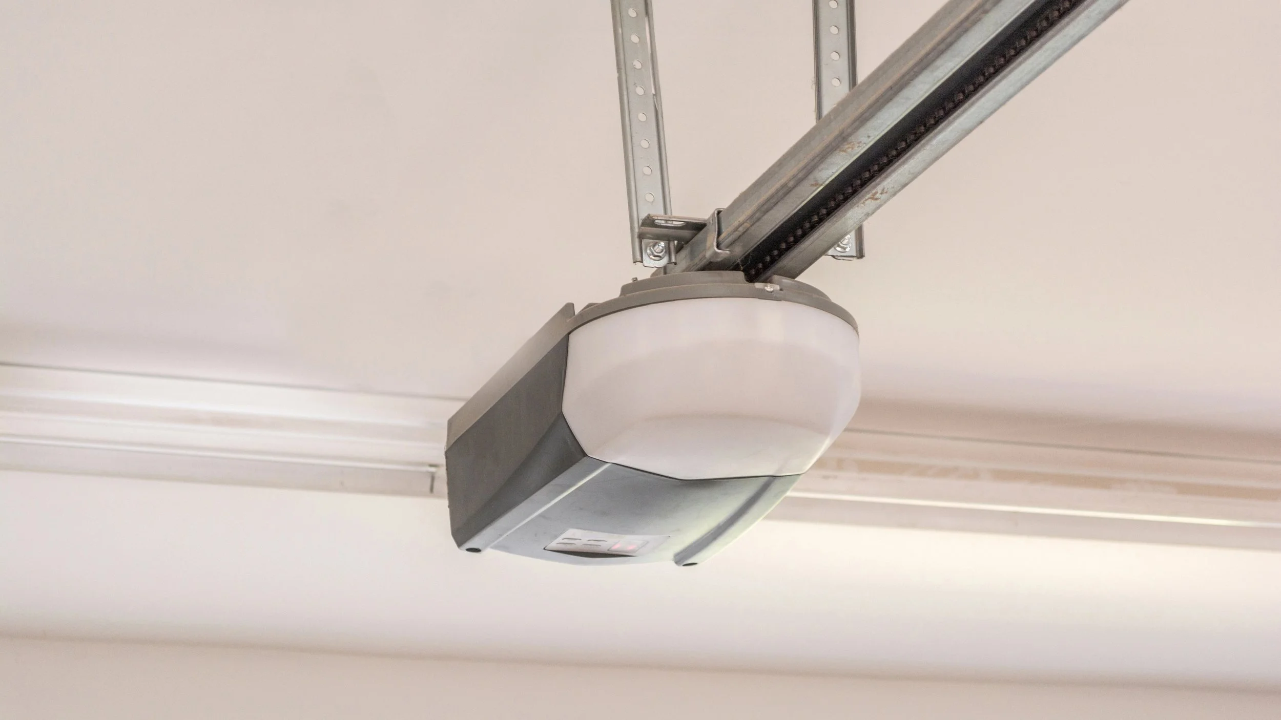 A garage door opener attached to the ceiling with metal rails and a white plastic cover.