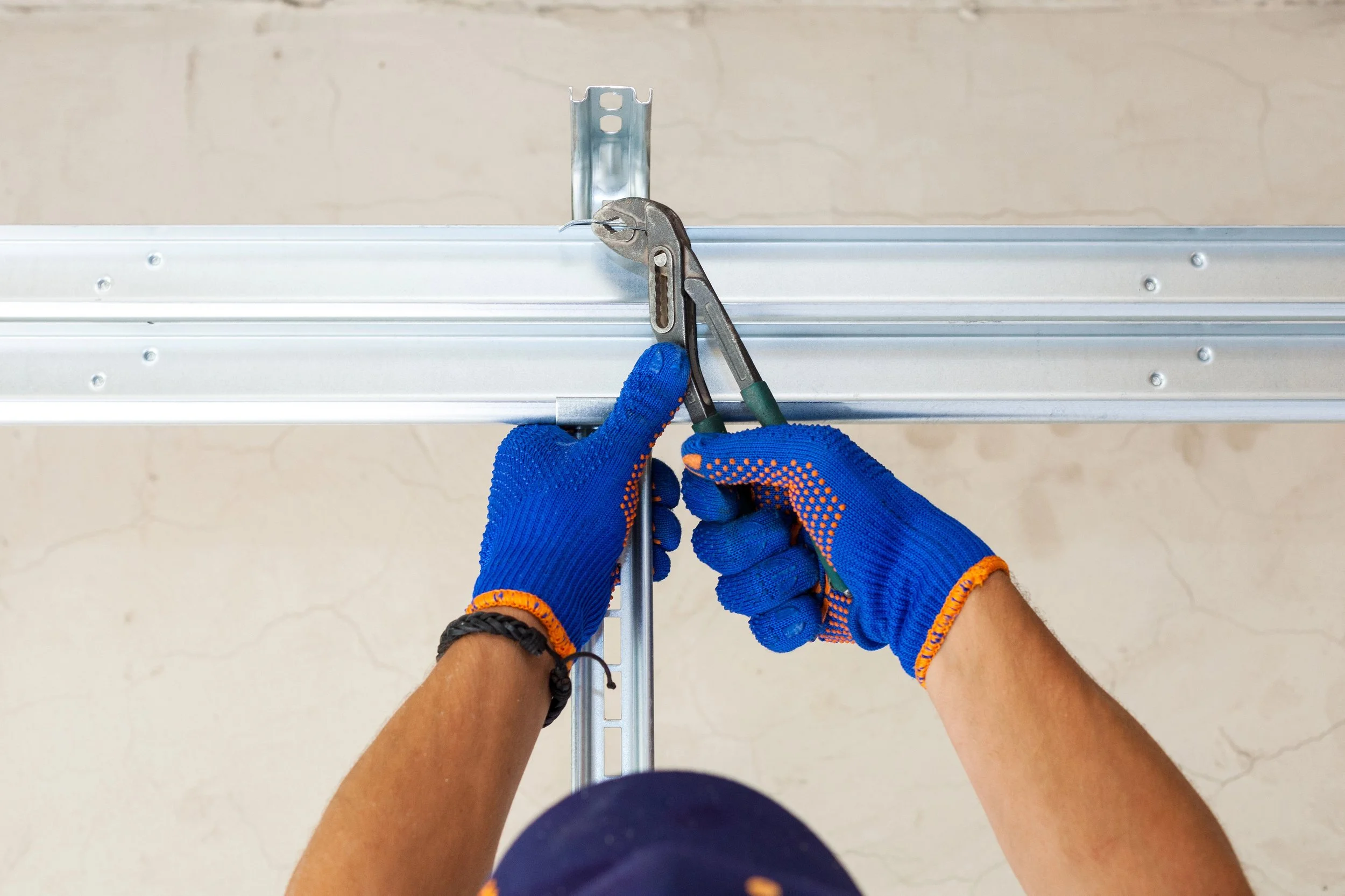 Hands wearing blue gloves assembling a metal frame with a wrench and pliers.