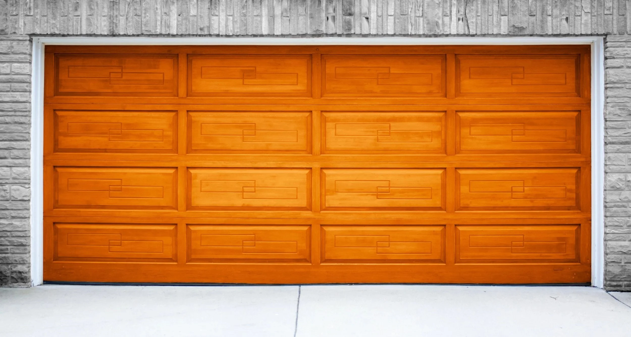 A wooden garage door with rectangular details, framed by a brick wall with white trim at the sides and top.