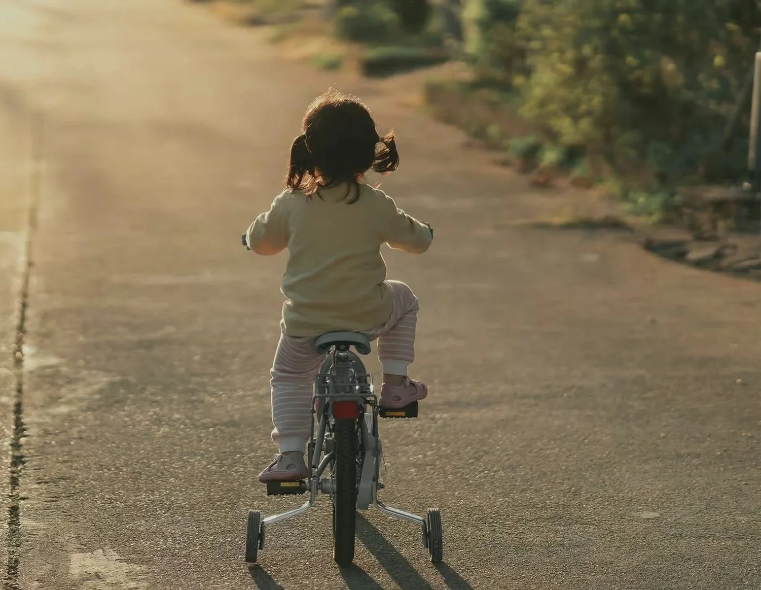 Young girl riding a bicycle on a paved road during sunset