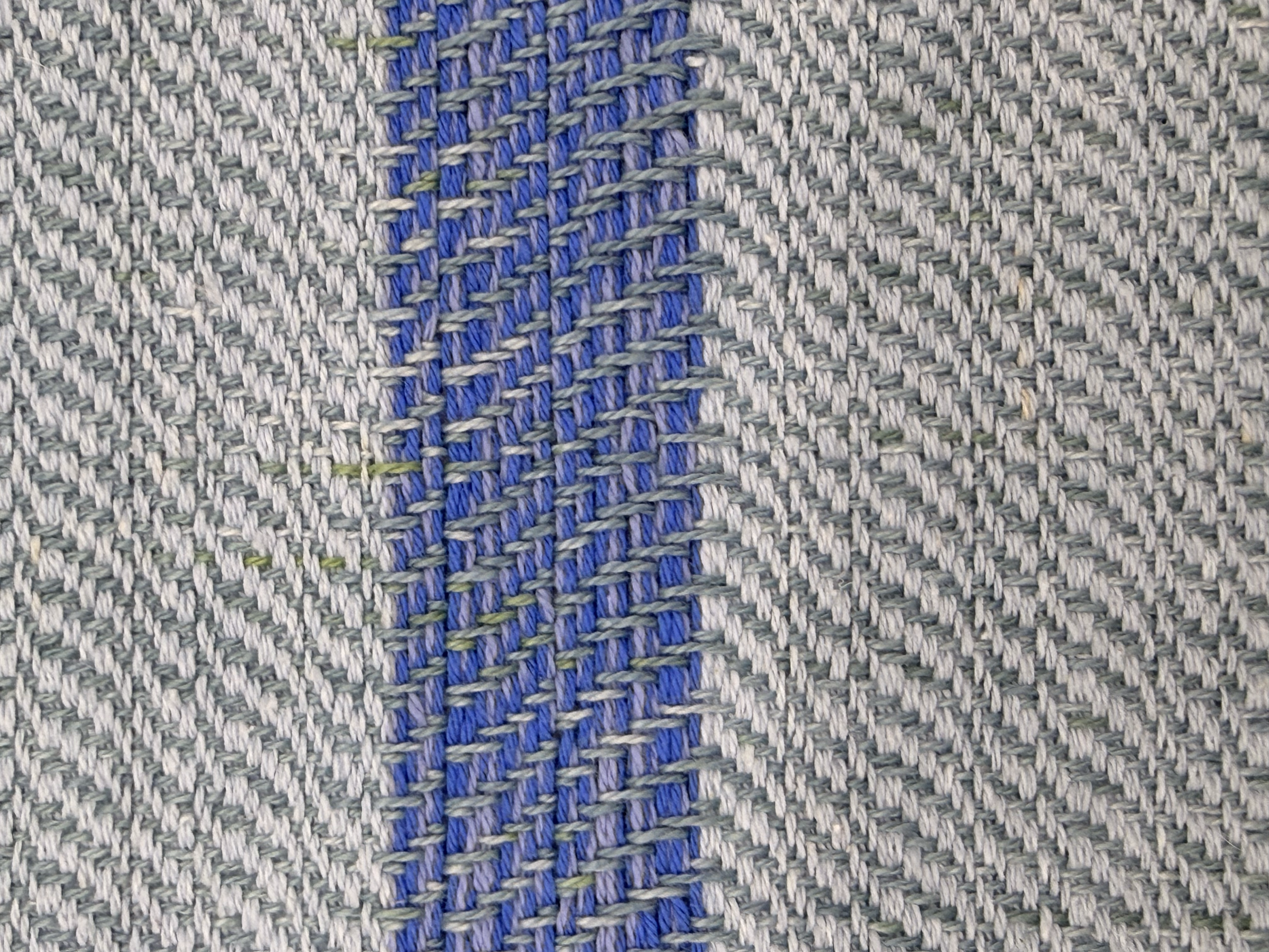 Close-up of a woven fabric with a pattern of blue, gray, and white threads forming a stripe design.
