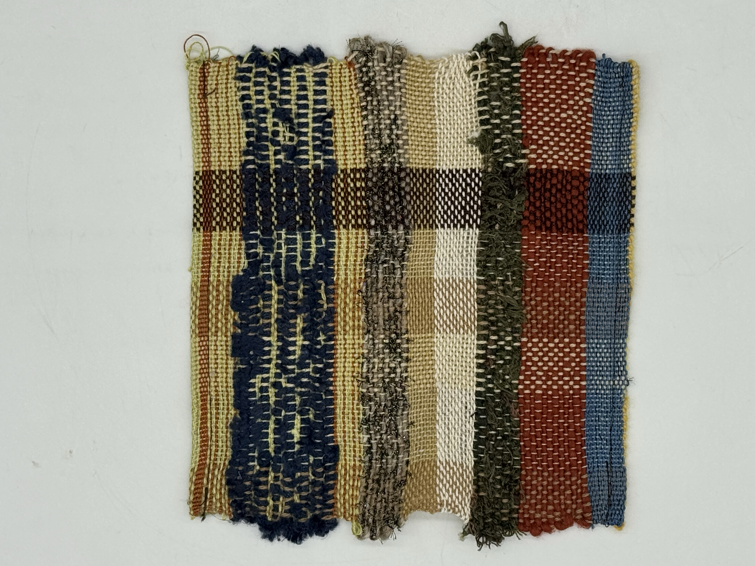 A woven textile with vertical stripes in blue, yellow, brown, beige, black, red, and blue, featuring various woven patterns and textures.