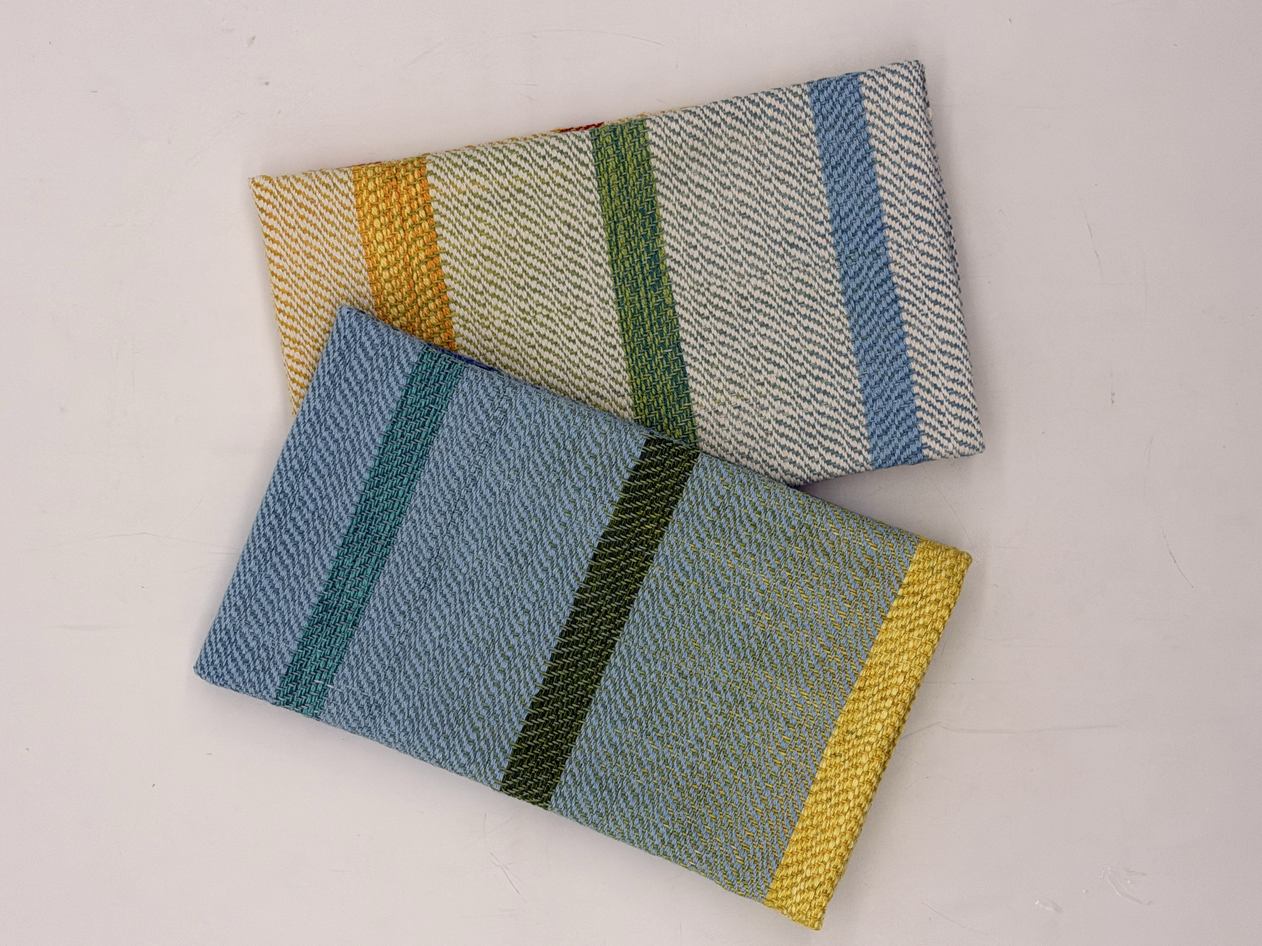 Folded fabric or cloth with multi-colored stripes in yellow, orange, green, blue, and yellow, lying on a white surface.