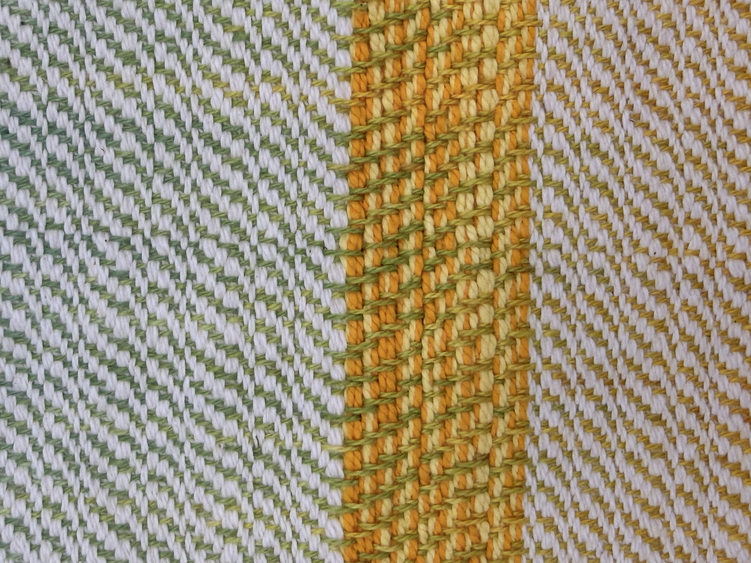 Close-up of woven fabric with white, green, yellow, and orange threads creating a striped pattern.