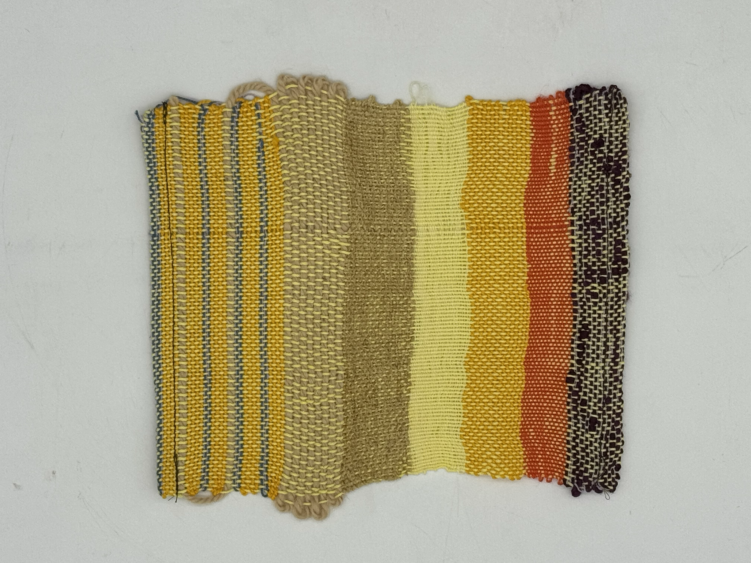 A patch of woven fabric with striped and solid patterns in yellow, gold, orange, and brown colors.