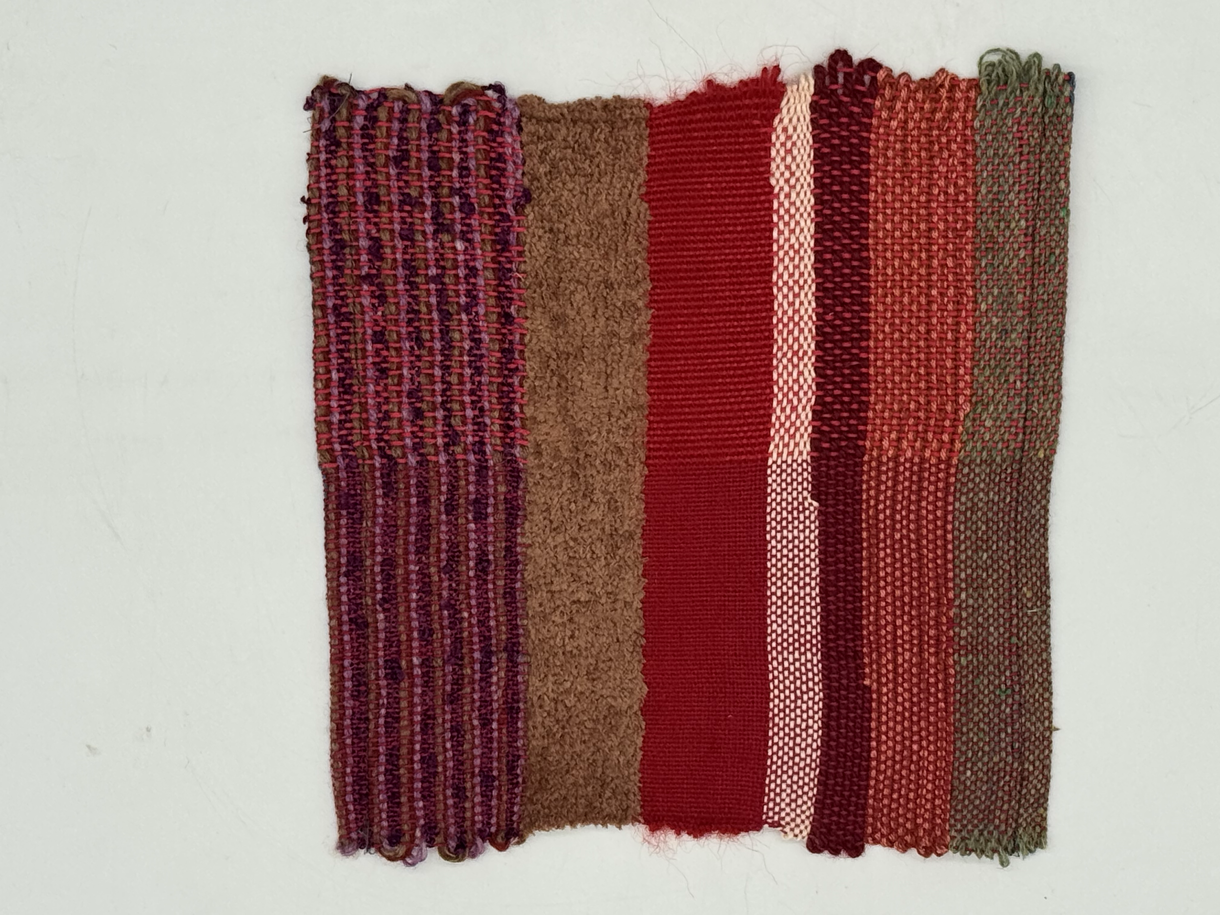 A vertical strip of woven fabric with multiple colors, including purple, brown, red, pink, and green, arranged in different patterns.