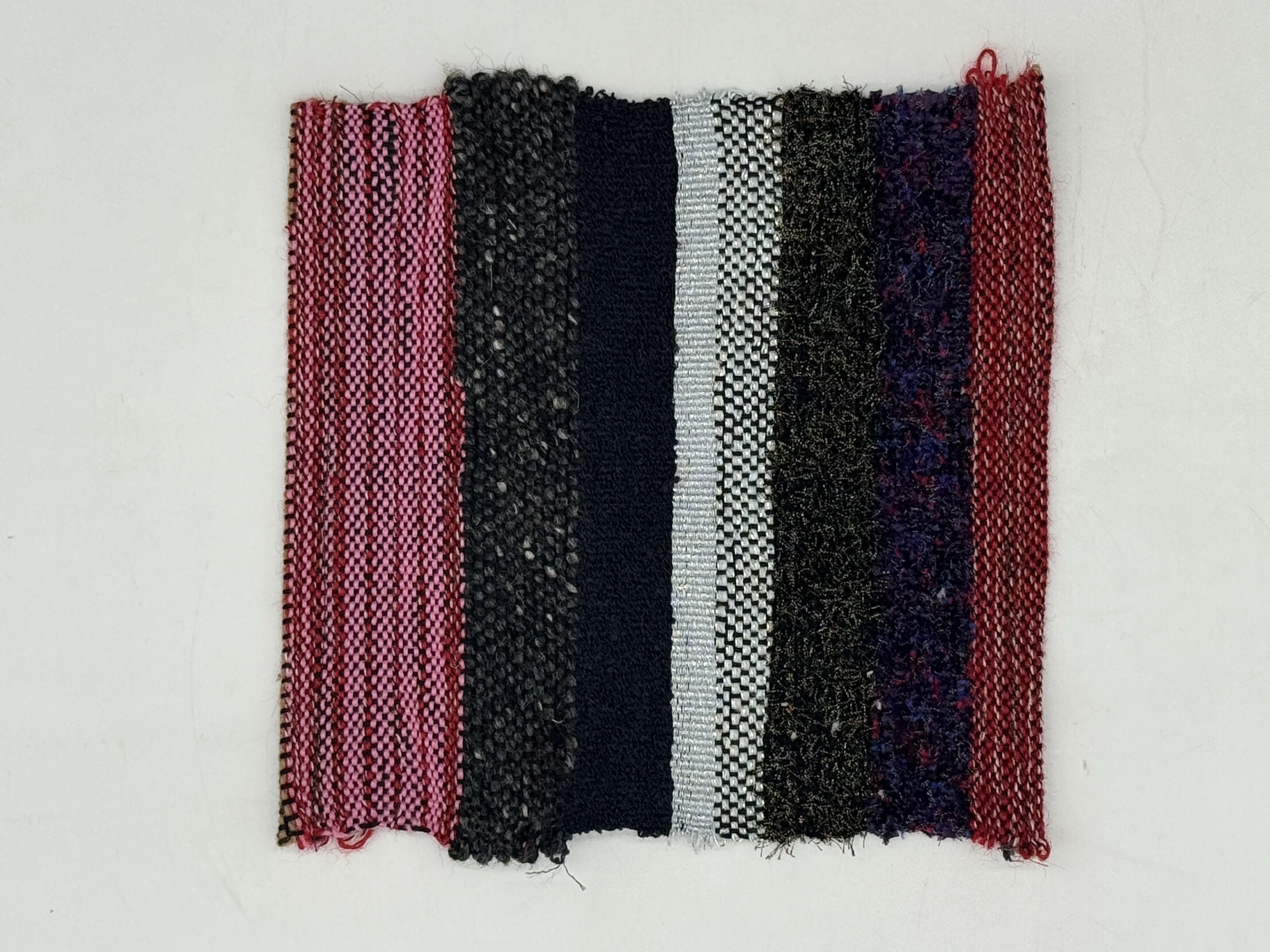 A textile swatch with vertical stripes in various colors and patterns, including pink, black, silver, and purple.