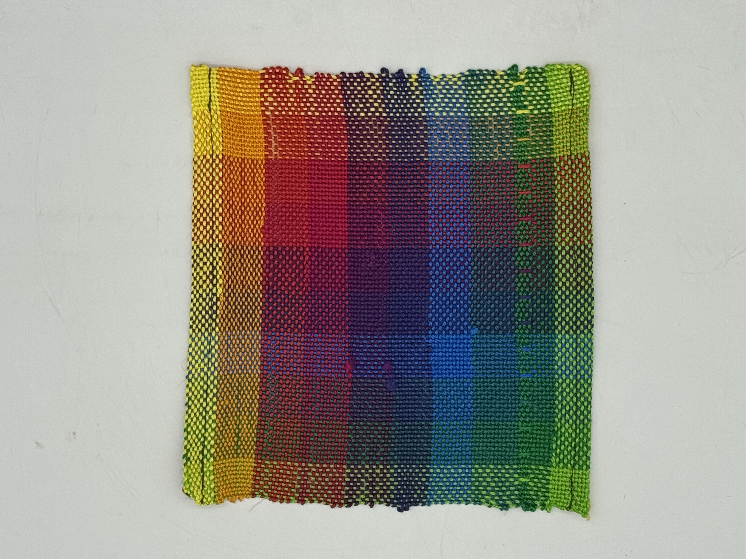 A small square piece of rainbow-colored woven fabric on a white background, with horizontal stripes of rainbow colors.