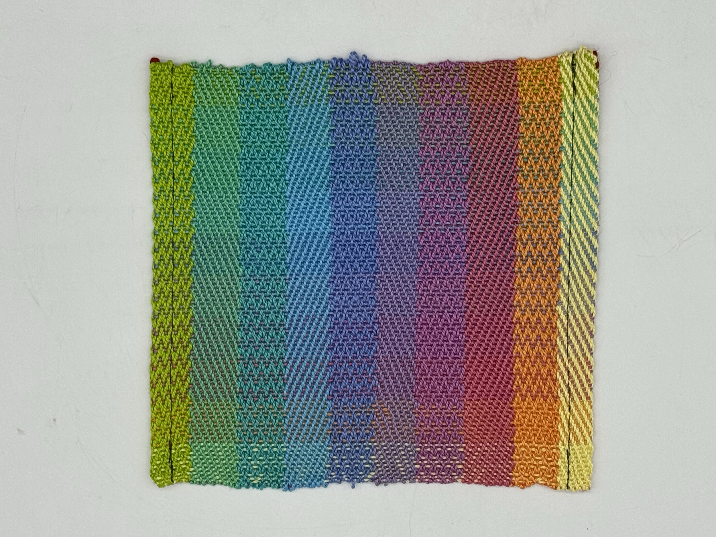 A close-up of a colorful woven fabric with rainbow stripes in various colors including green, blue, purple, pink, orange, and yellow.